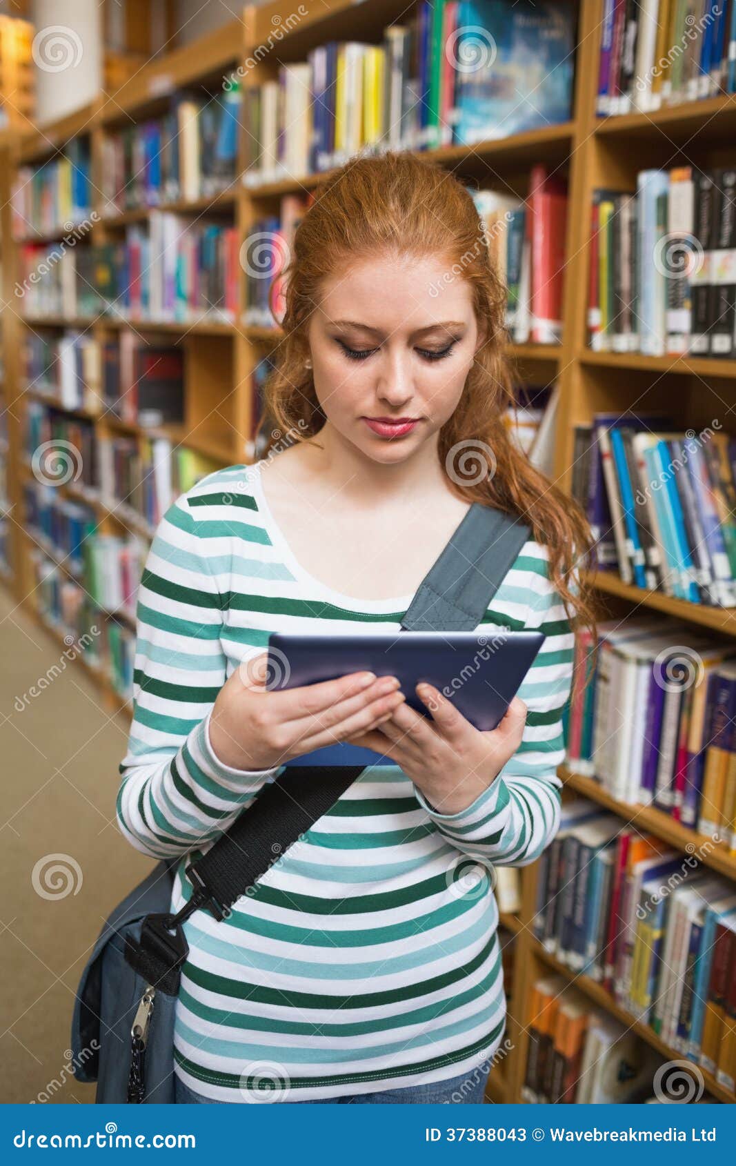 redhead student using tablet standing in library