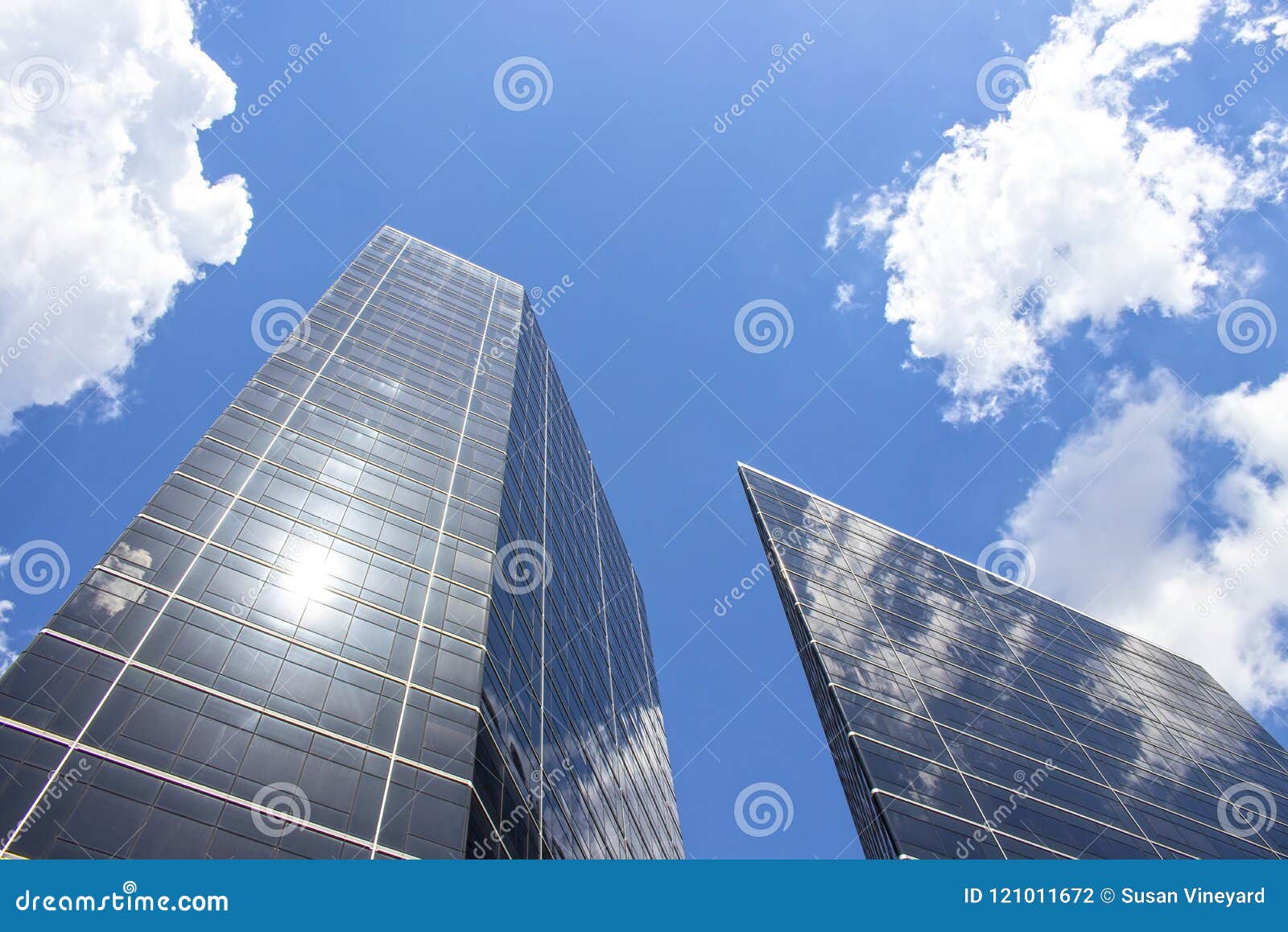reflection of sky and clouds on tall modern skyscrapers looking up with lens flare