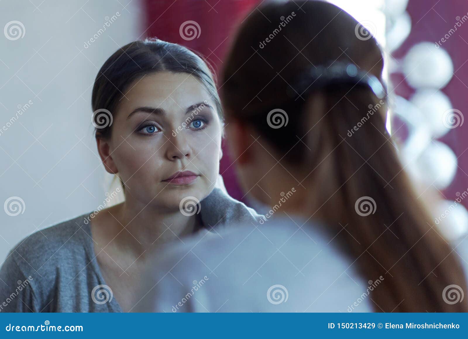reflection of a young attractive caucasian woman looking into a mirror. wearing casual, beautiful blue eyes, serious look.