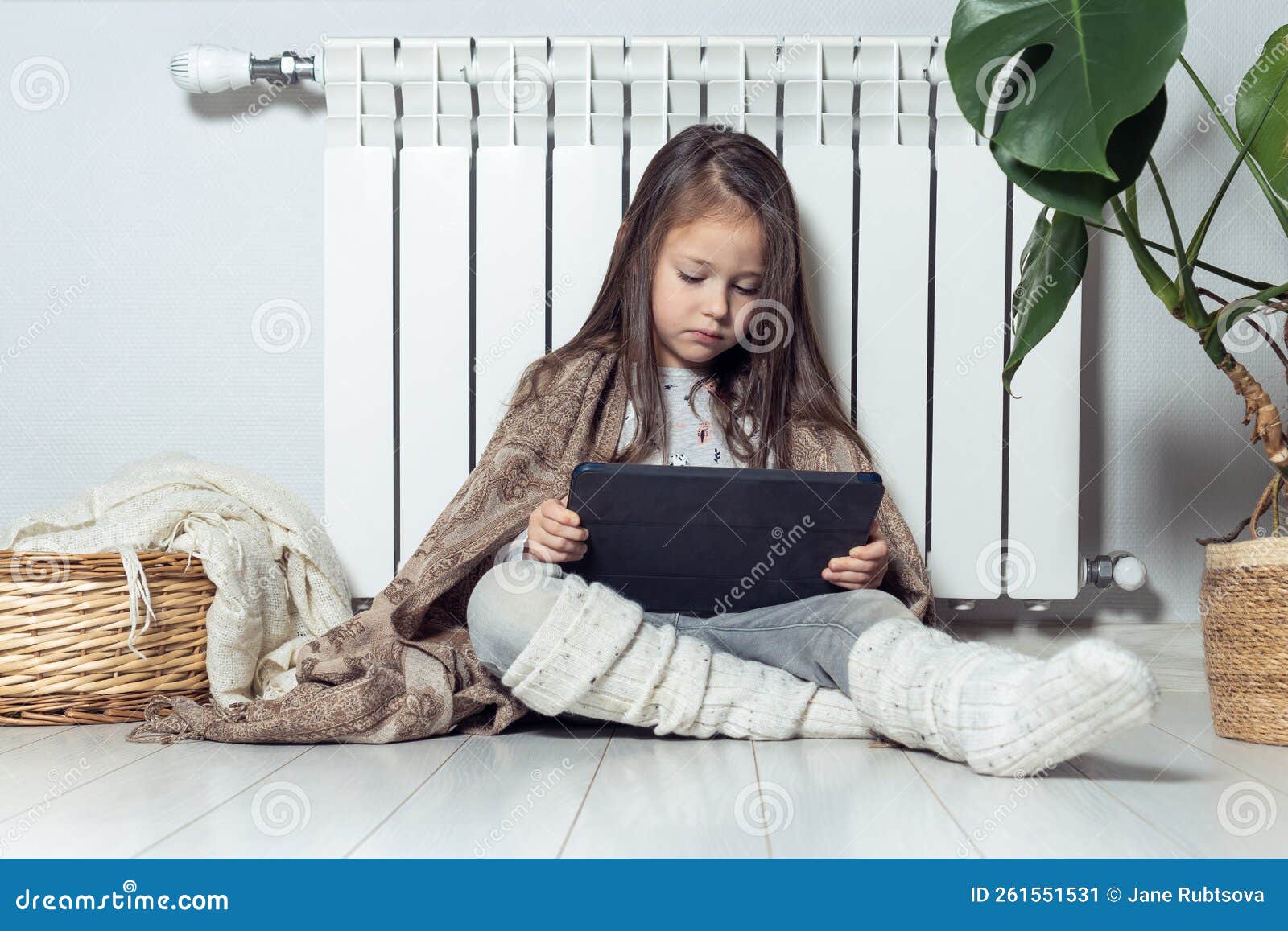 Relaxed Little Brunette Long Haired Girl Use Electronic Tablet, Live Streaming Online, Blogging, Vlogging Near Radiator Stock Image
