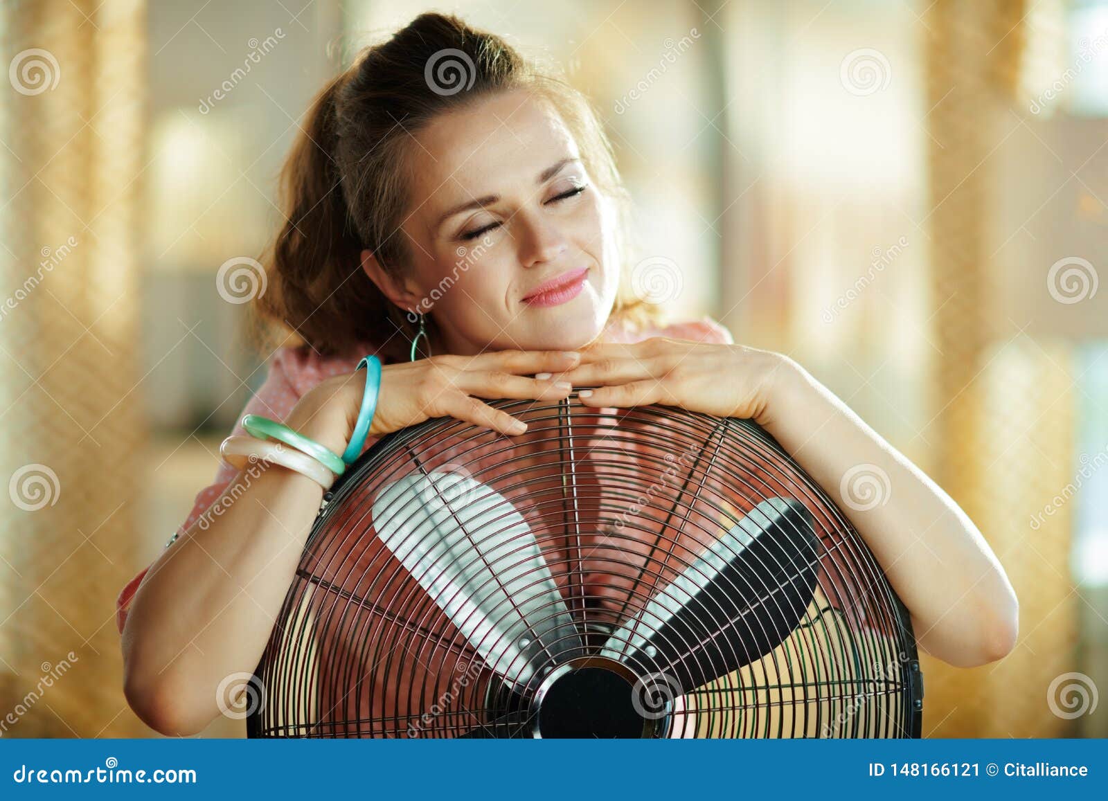 Relaxed Stylish Woman Embracing Metallic Floor Standing Fan Stock Image