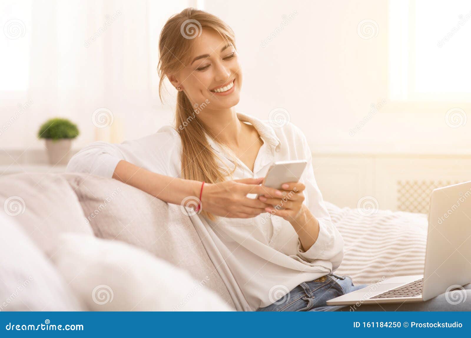 Relaxed Woman Using Smartphone Sitting with Laptop on Couch Indoor ...