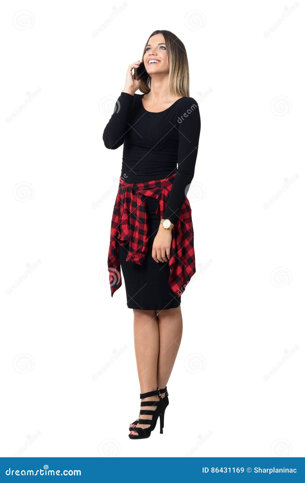 Relaxed young stylish girl in black dress laughing on the phone looking up. Full body length isolated over white studio background.