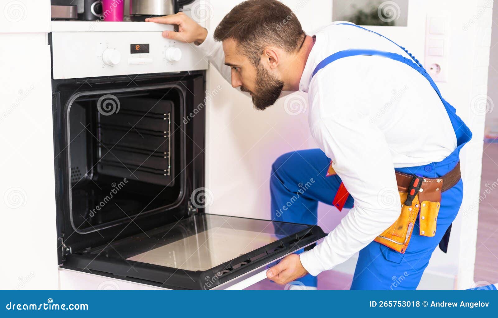 Repairman Examining Oven With Screwdriver In Kitchen With Tool Case