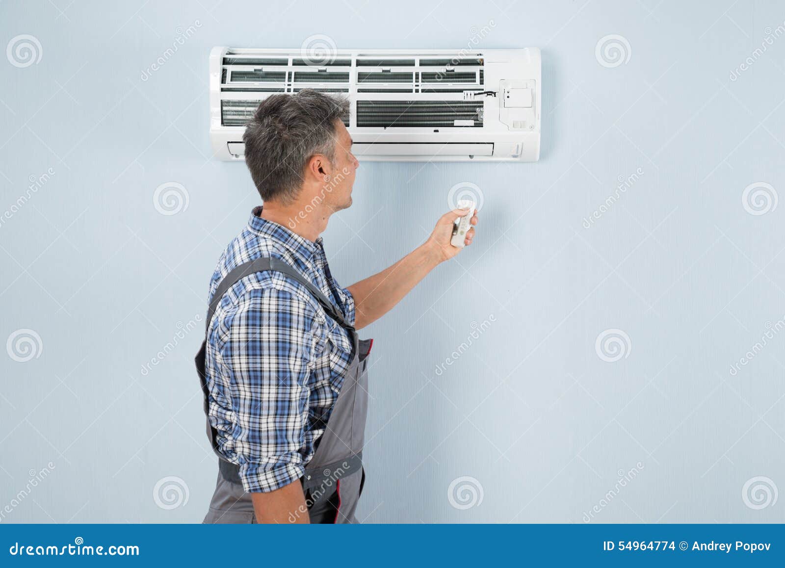 Repairman Operating Air Conditioner with Remote Controller Stock Photo