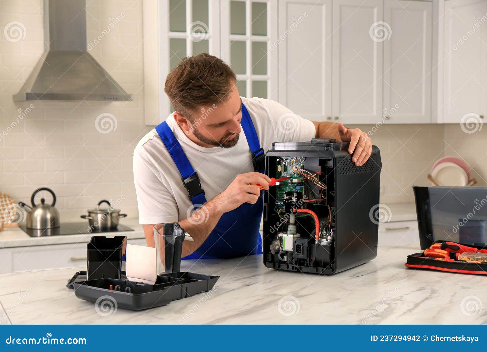 Repairman with Screwdriver Fixing Coffee Machine at Table in Kitchen