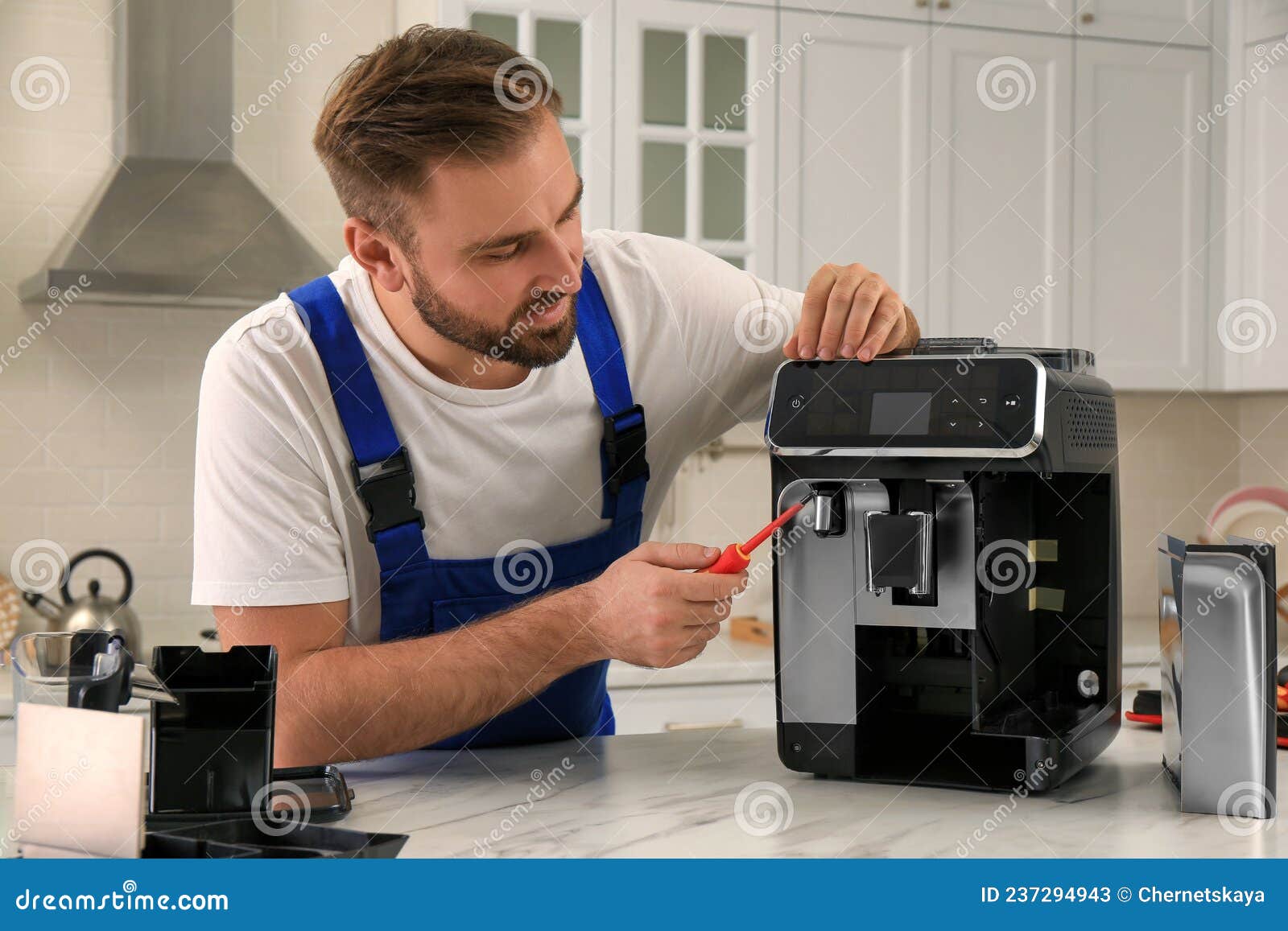 Repairman with Screwdriver Fixing Coffee Machine at Table in Kitchen