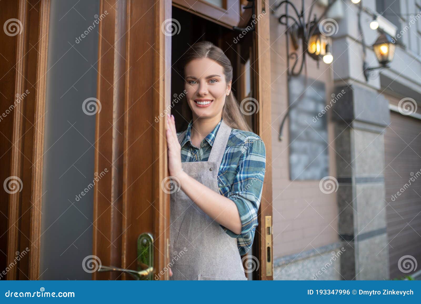 Cheerful Young Waitress in Grey Apron Opening Wooden Door Stock Photo ...