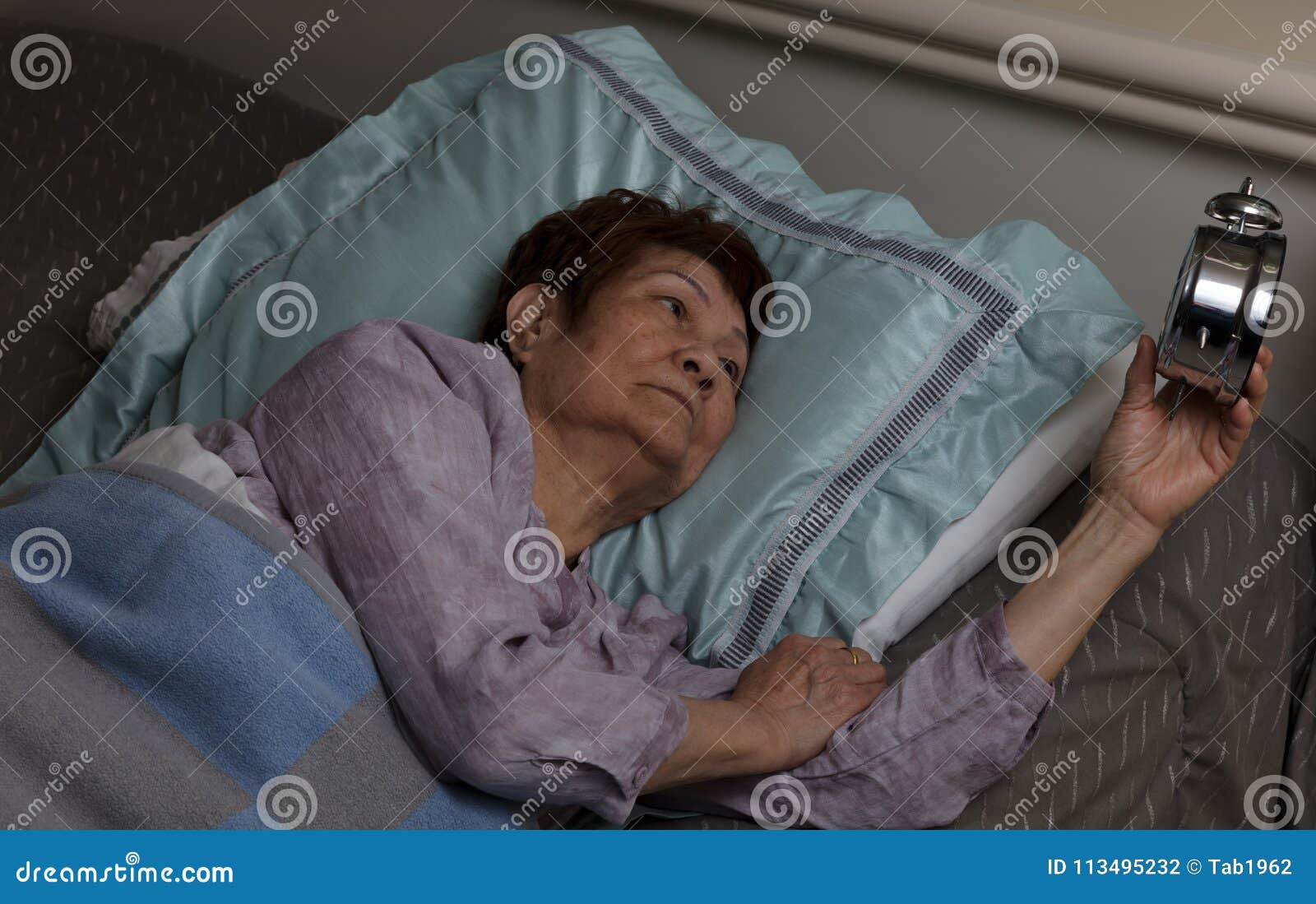 restless senior woman glaring at alarm clock during nighttime while in bed