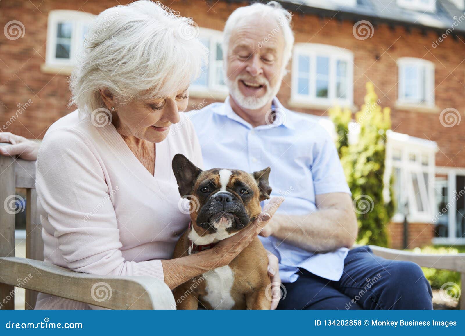 retired couple sitting on bench with pet french bulldog in assisted living facility