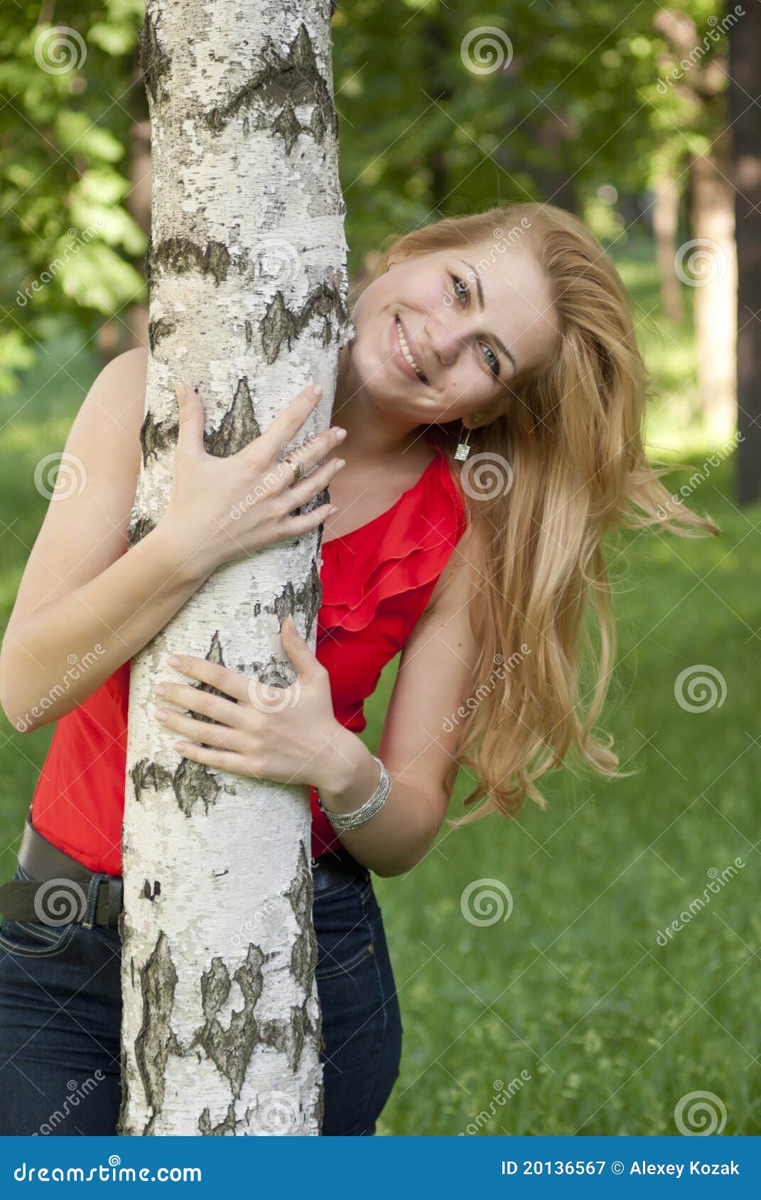 Retrato de la muchacha en una blusa roja que sonríe y abraza un abedul.