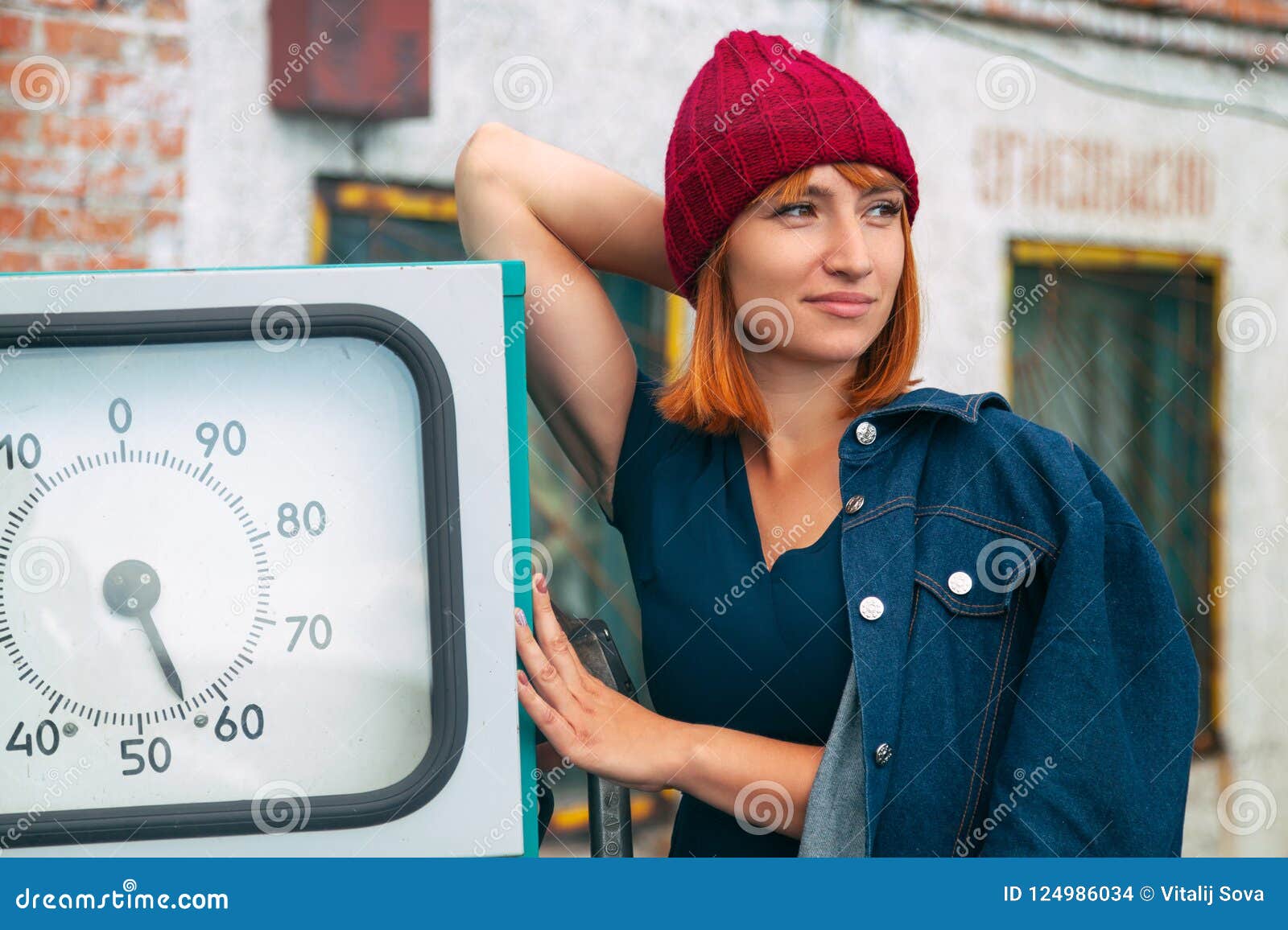 Foto atmosférica al aire libre de la forma de vida de la mujer pelirroja hermosa joven en sombrero que hace punto en día soleado del otoño en la vieja gasolinera Retrato de la mujer alegre