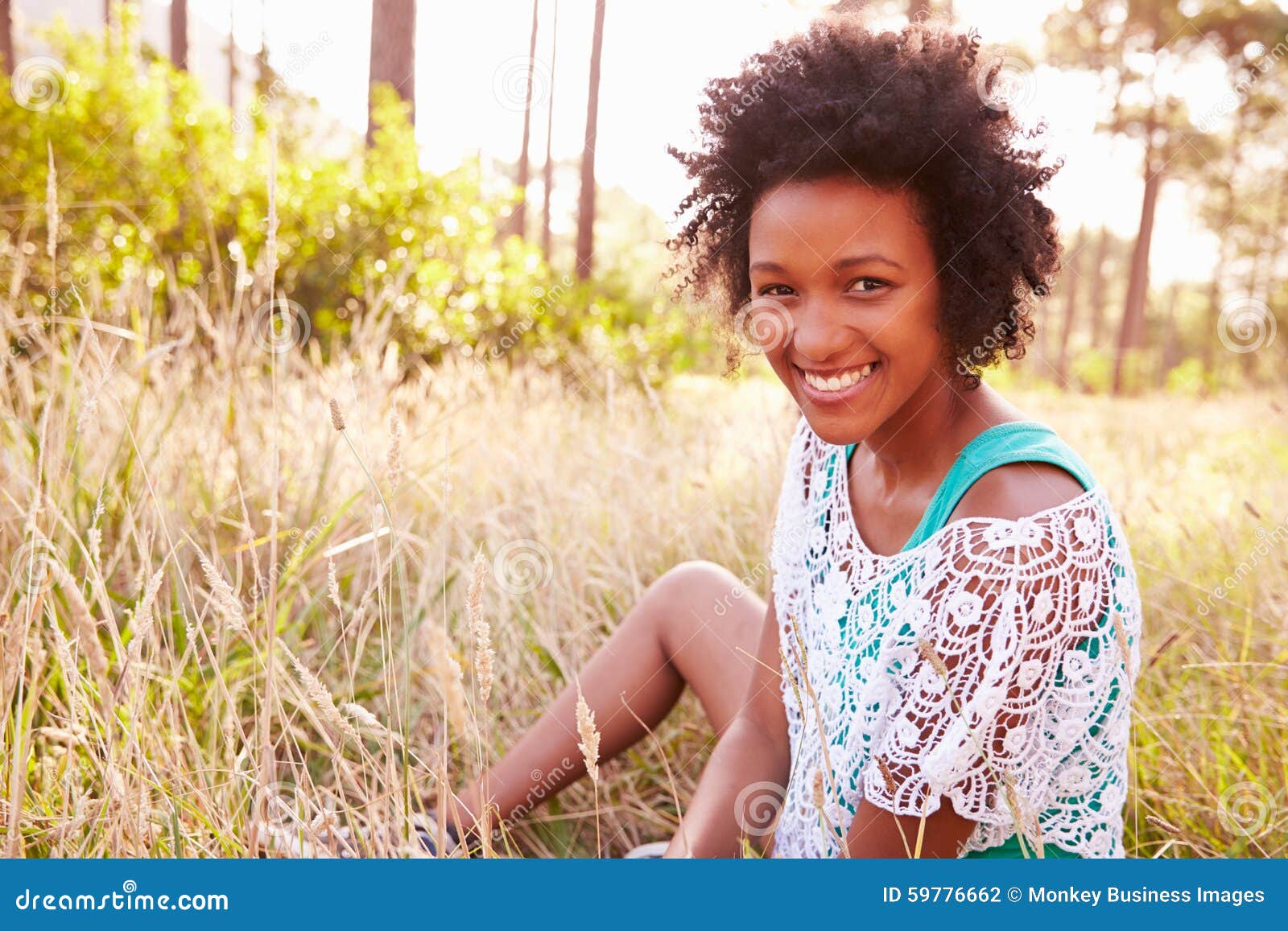 Retrato de la mujer joven sonriente que se sienta en campo