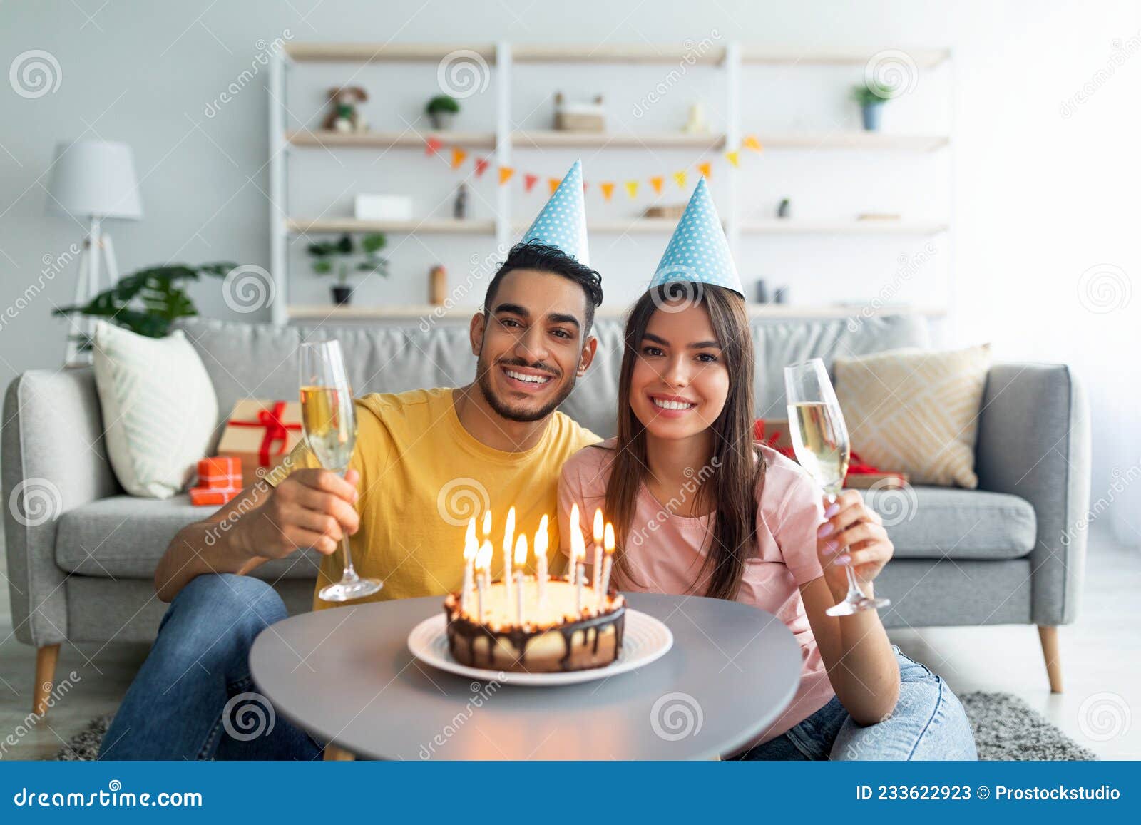 Retrato De Pareja Interracial En Sombreros De Fiesta Sosteniendo Gafas De  Champán Frente a Torta De Cumpleaños Con Velas En Casa Imagen de archivo -  Imagen de oriente, acontecimiento: 233622923