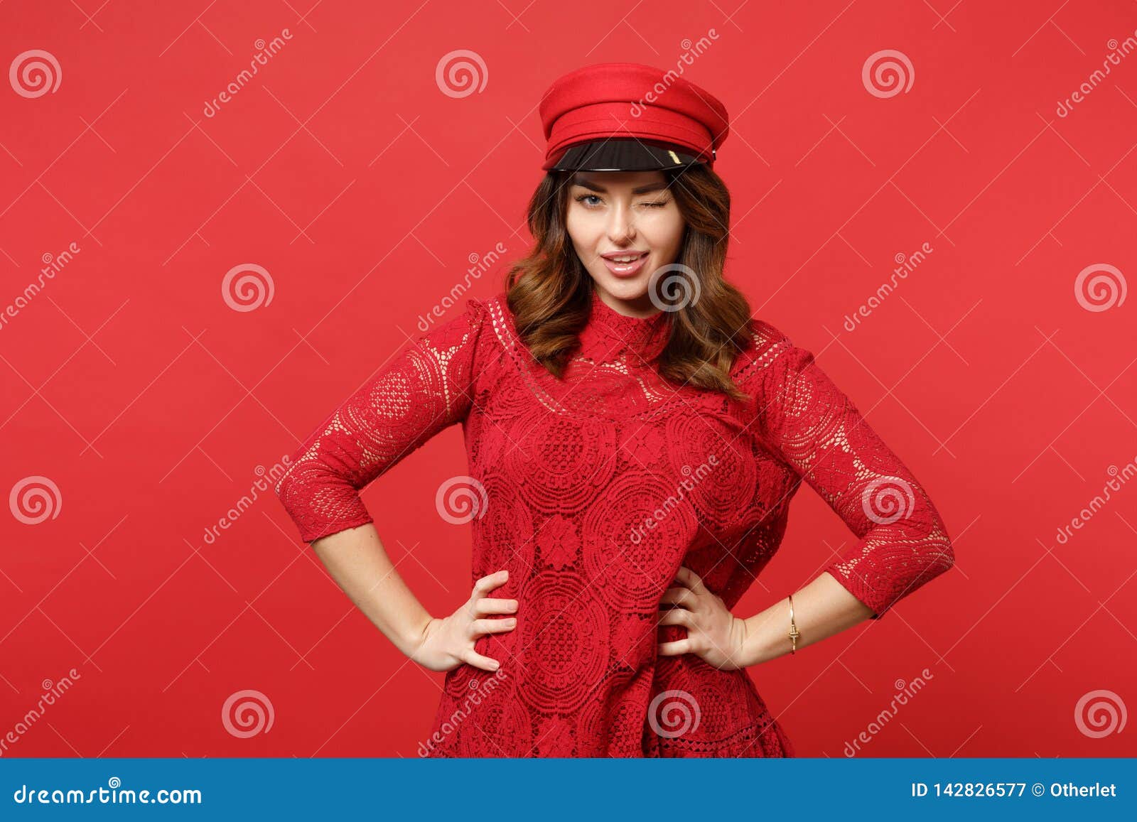 Retrato de piscar a jovem mulher bonita no vestido do laço, posição do tampão com akimbo dos braços isolado na parede vermelha br. Retrato de piscar a jovem mulher bonita no vestido do laço, posição do tampão com akimbo dos braços isolado no fundo vermelho brilhante da parede no estúdio Emoções sinceras dos povos, conceito do estilo de vida Zombaria acima do espaço da cópia