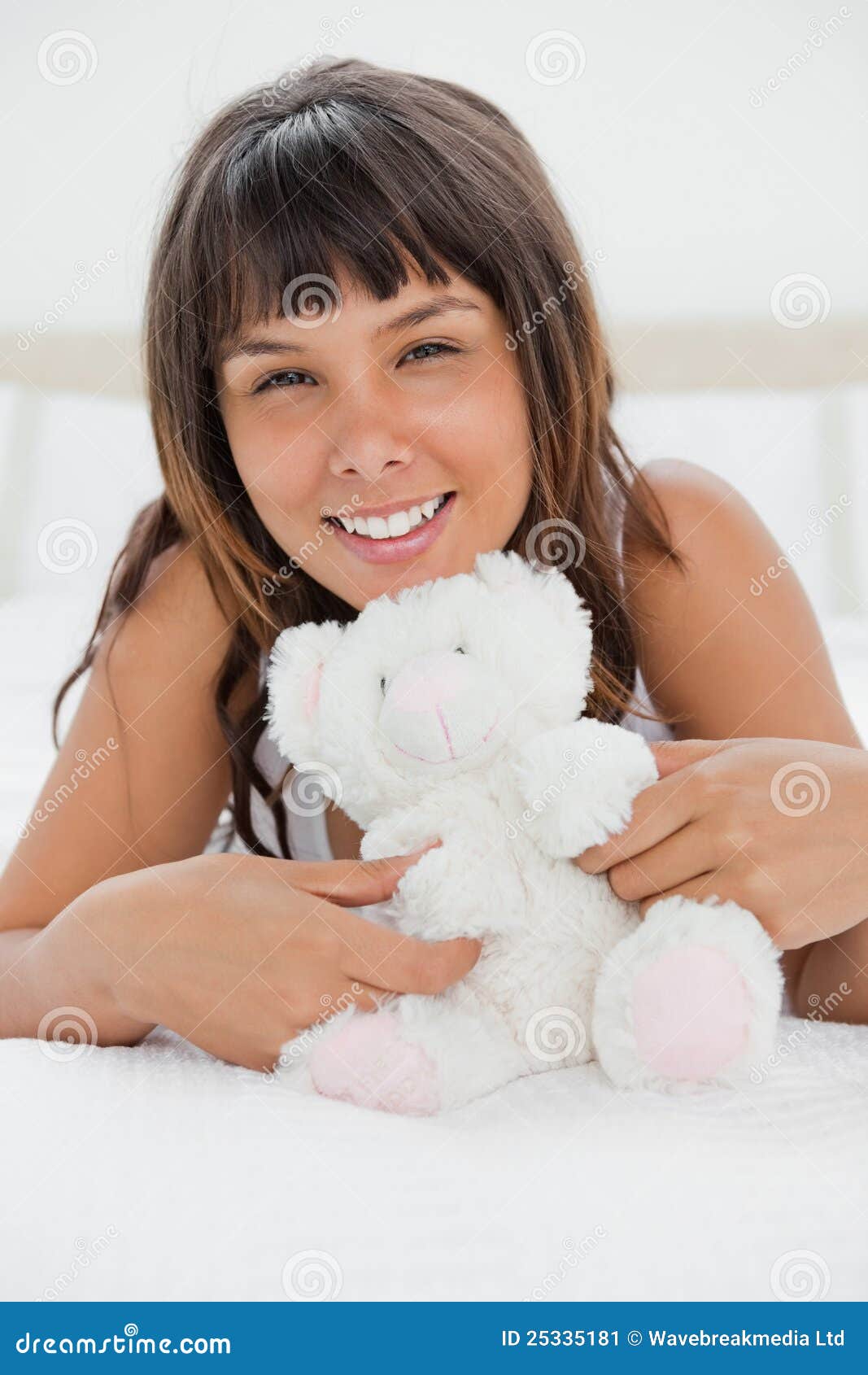 Retrato de uma jovem mulher que joga com um urso de peluche em sua cama