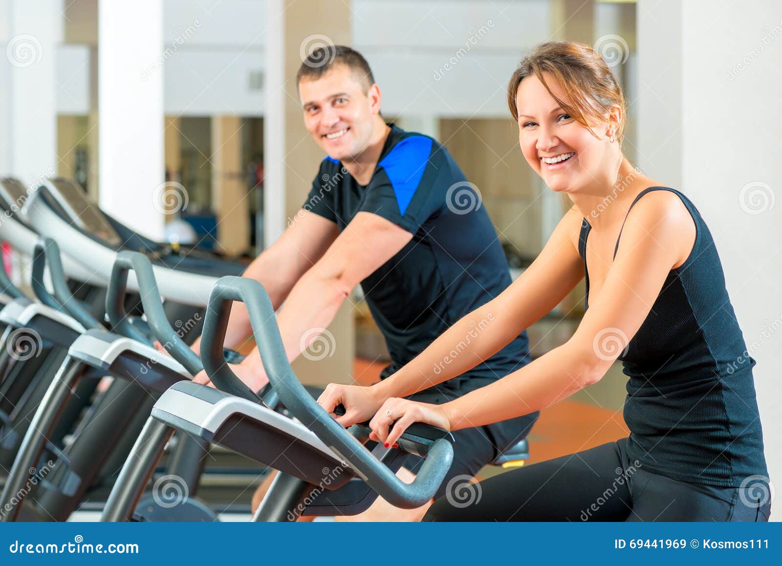 Retrato de un par feliz en una bici inmóvil en el gimnasio