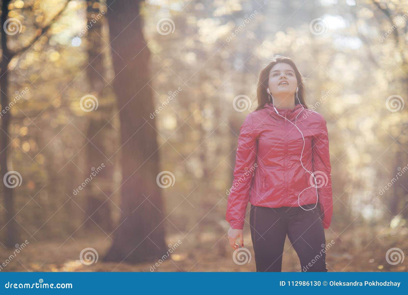 Retrato de una muchacha que entrena y escucha la música en el parque del otoño de la mañana. Retrato de una muchacha que entrena y escucha la música en auriculares en el parque del otoño de la mañana Luz de la buena mañana Se divierte tema