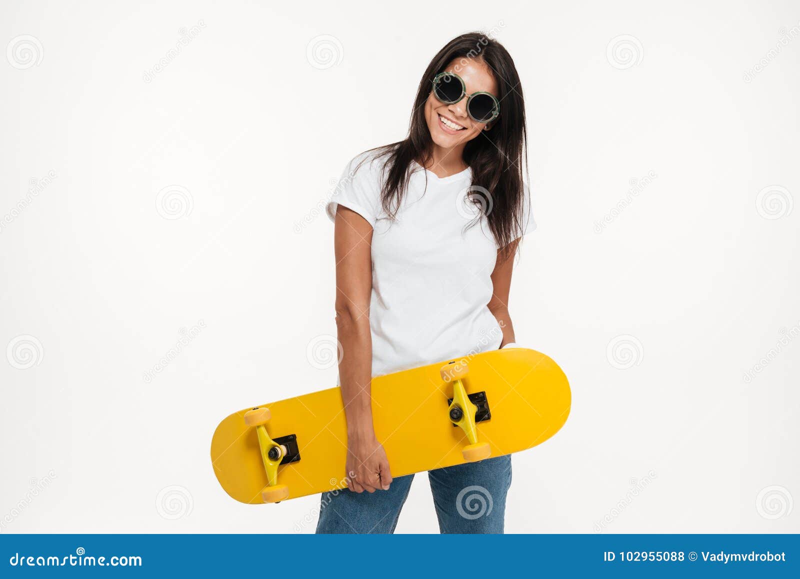 Retrato de una mujer alegre feliz que sostiene el monopatín mientras que coloca y mira la cámara aislada sobre el fondo blanco