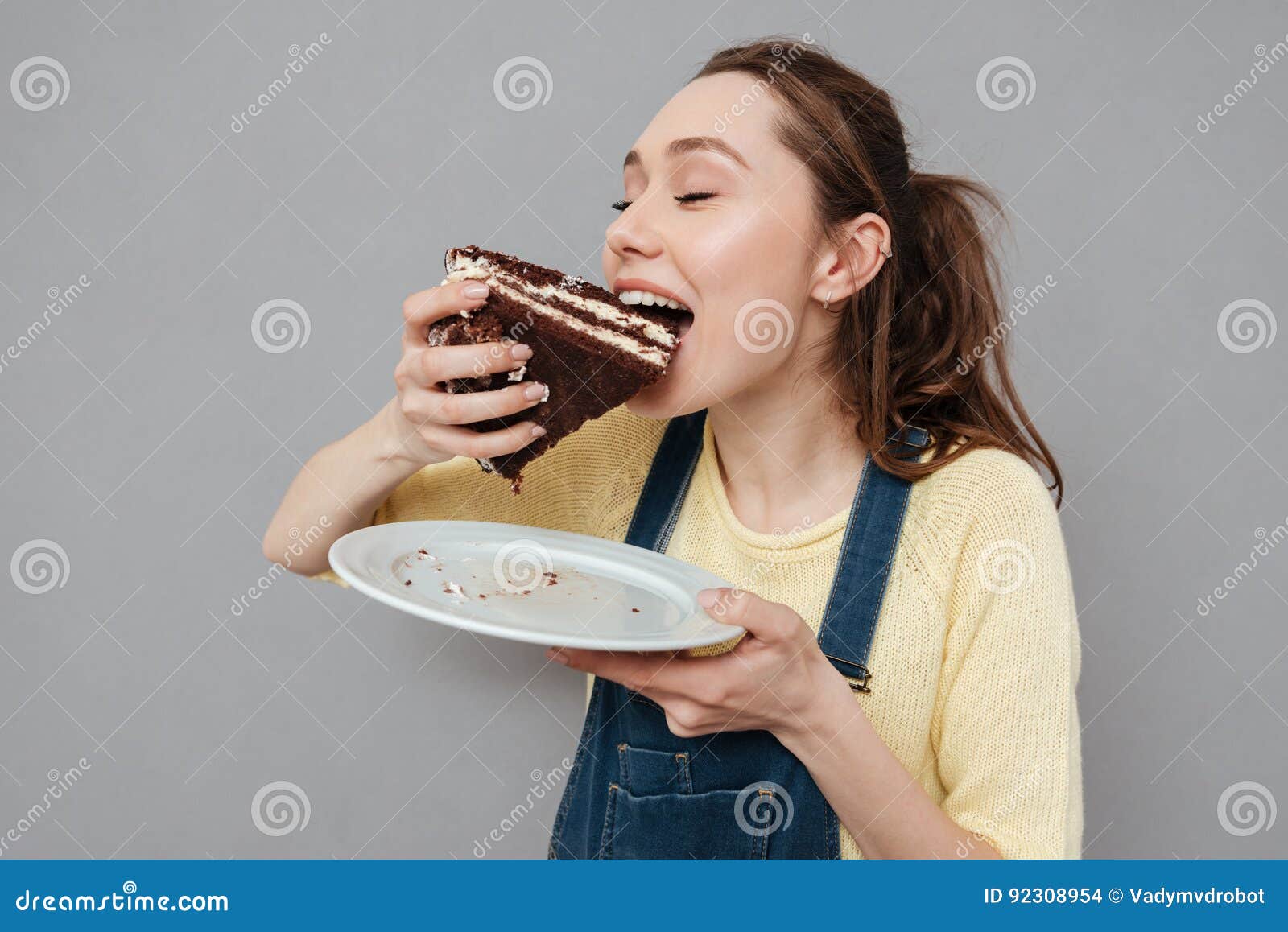 Retrato de una mujer embarazada hambrienta que come la torta de chocolate dulce. Retrato de una mujer embarazada feliz hambrienta que come la torta de chocolate dulce aislada en un fondo gris