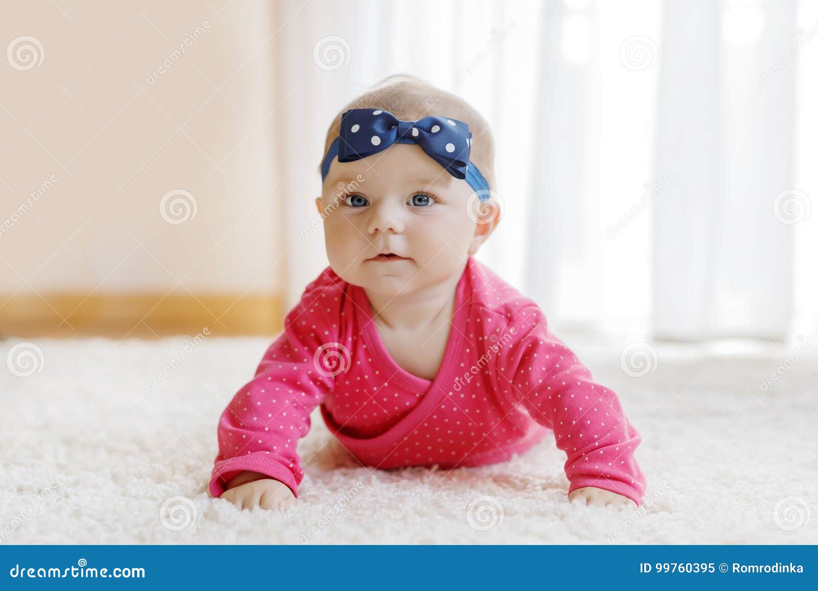 Retrato del pequeño bebé minúsculo de 5 meses dentro en casa. Bebé con los ojos azules que mienten en el vientre Cuarto de niños para los niños Materia textil y lecho para los niños Muchacha recién nacida linda feliz niño con la venda
