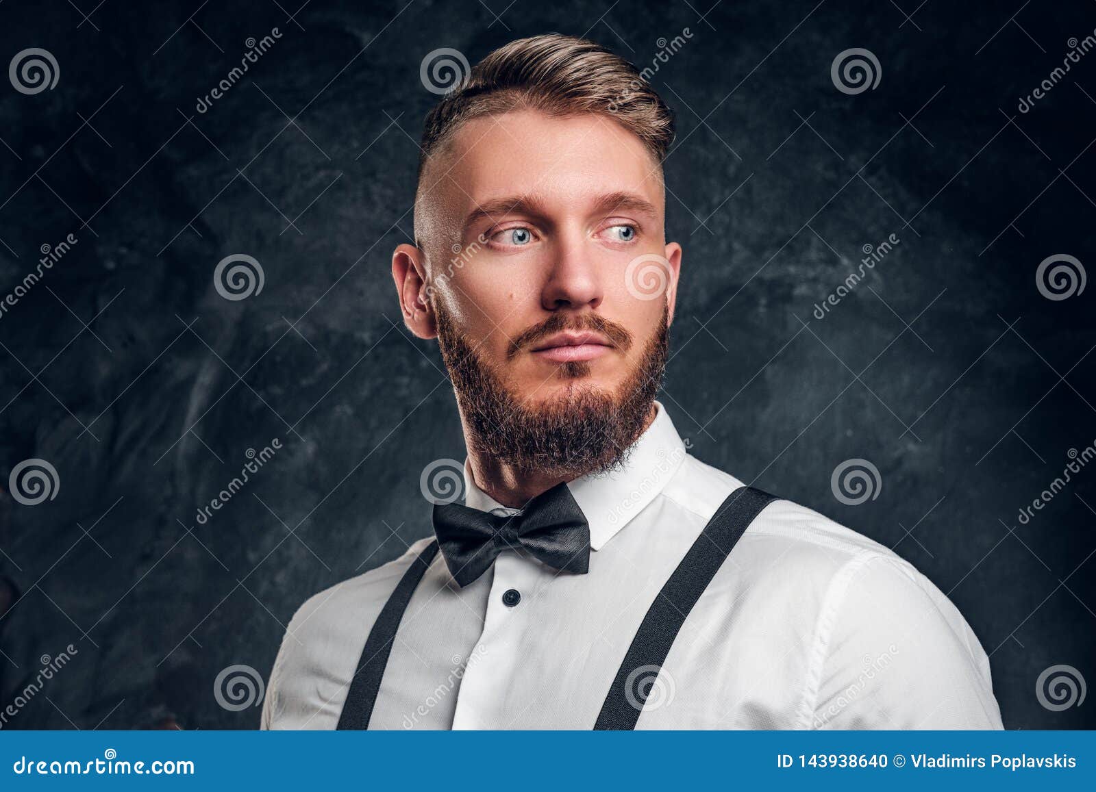 Retrato do close up de um homem com barba à moda e do cabelo na camisa com laço e suspensórios Foto do estúdio contra a obscurida. Retrato do close up de um homem com barba à moda e do cabelo na camisa com laço e suspensórios, olhando lateralmente Foto do estúdio contra o fundo escuro da parede