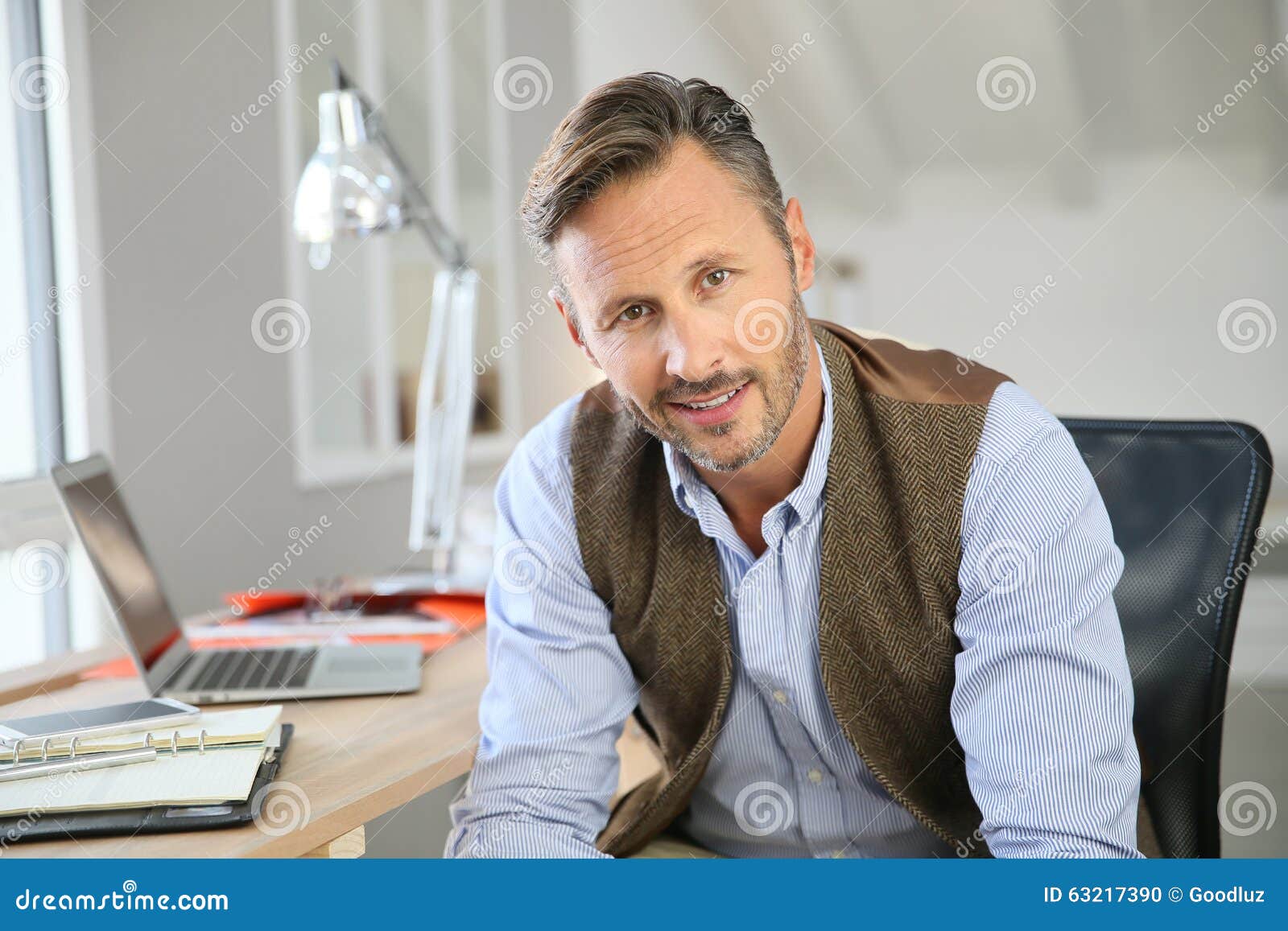 Retrato do homem de negócios de meia idade de sorriso no escritório. Homem considerável que senta-se no escritório
