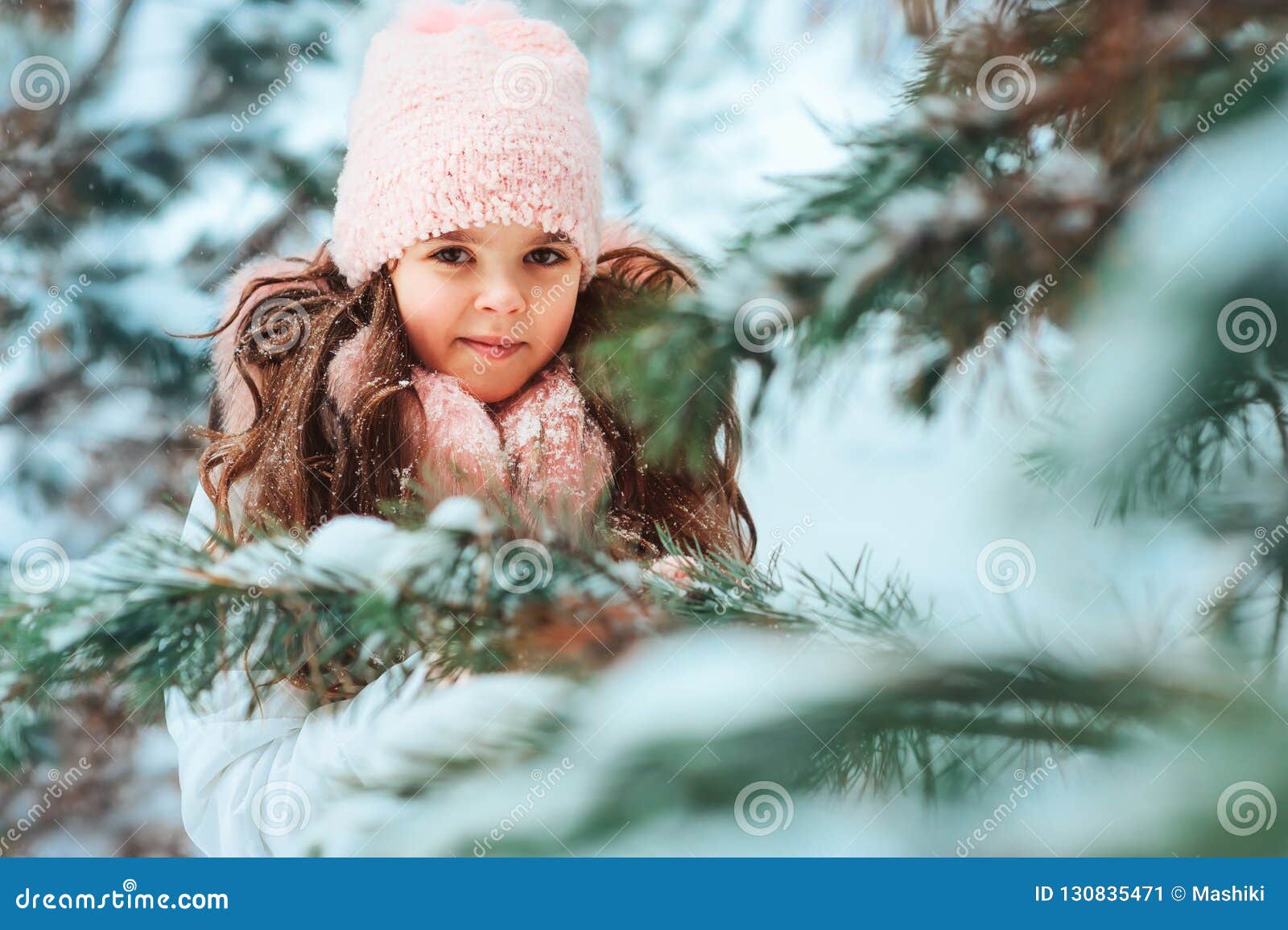 Retrato do inverno da menina feliz da criança no revestimento e no chapéu brancos e do jogo cor-de-rosa dos mitenes exterior na infância feliz da floresta nevado do inverno e no conceito ativo dos feriados de inverno