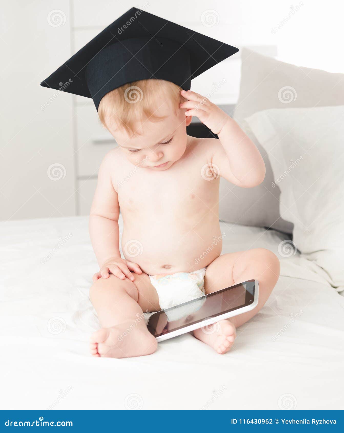 Retrato tonificado da testa vestindo da fricção do chapéu do professor do bebê bonito ao usar a tabuleta digital