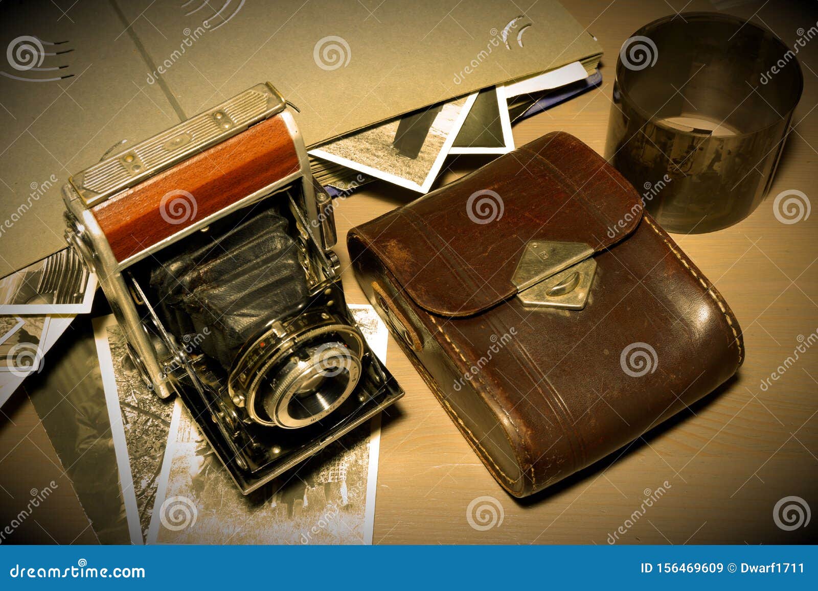 Retro old vintage outdated manual film camera circa 1940s, developed negative films, vintage photo album and leather camera case on wooden table. Vintage style sepia vignette photo.