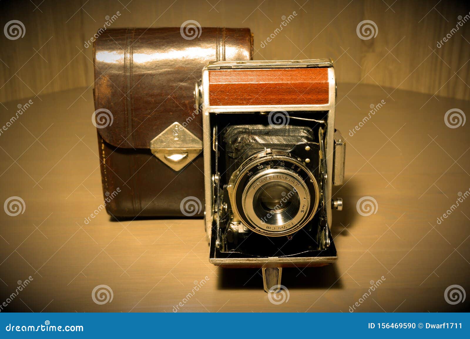 Retro old vintage outdated manual film camera circa 1940s and leather camera case on wooden table. Vintage style sepia vignette photo.