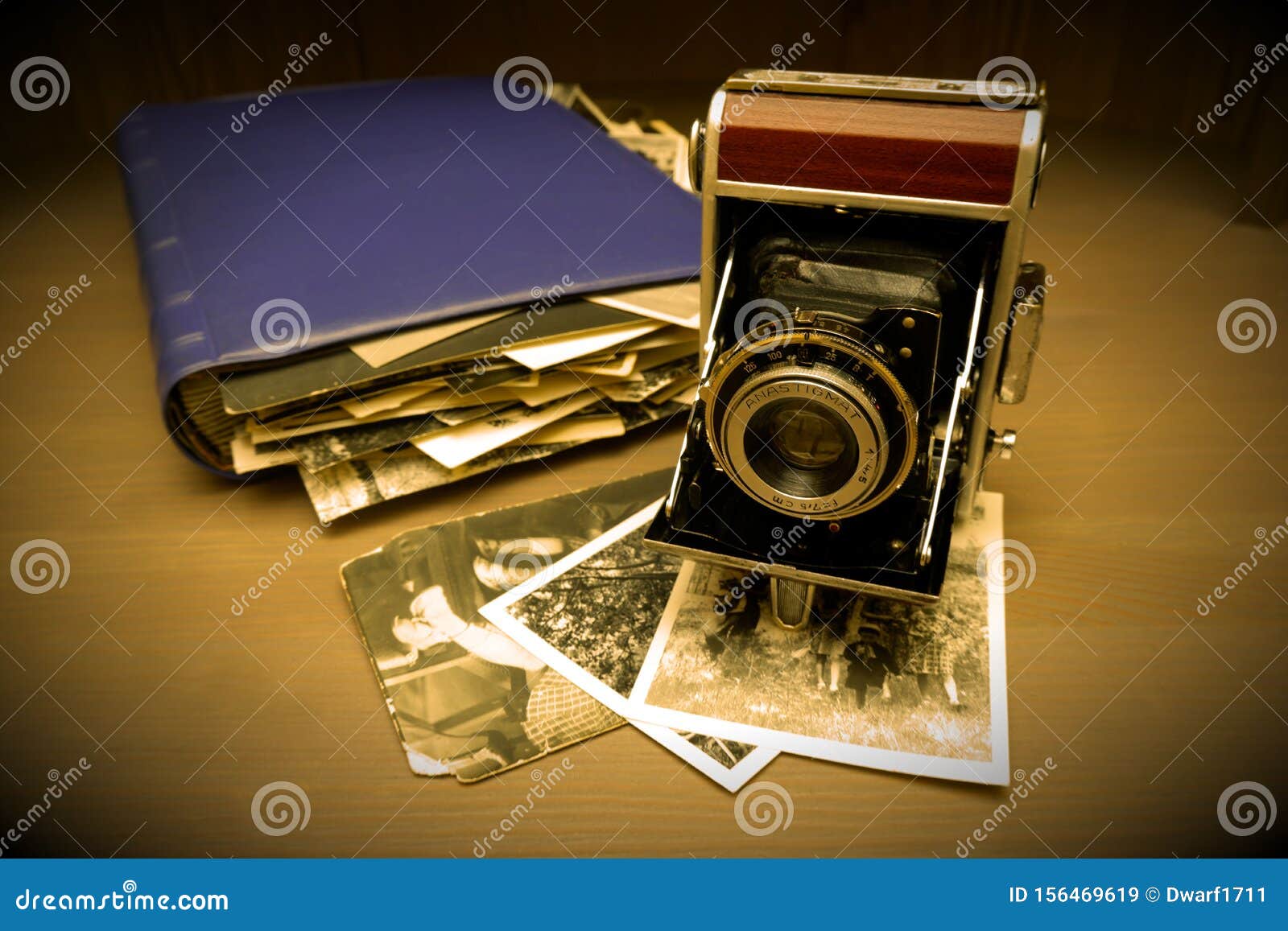 Retro old vintage outdated manual film camera circa 1940s, vintage photo album and old photos on wooden table. Vintage style sepia vignette photo.