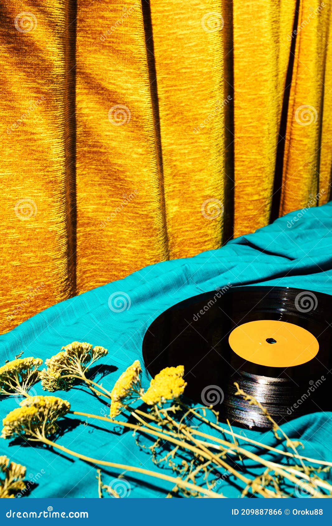 retro styled image of lp vinyl record on a cyan silk or saten fabric with dry old flowers and gold orange curtain in the