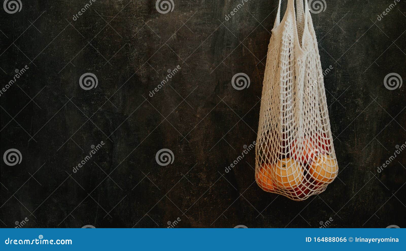 reusable mesh cottone bags hanging on the wall in house. eco friendly package for grocery with fruits on dark background. reusable