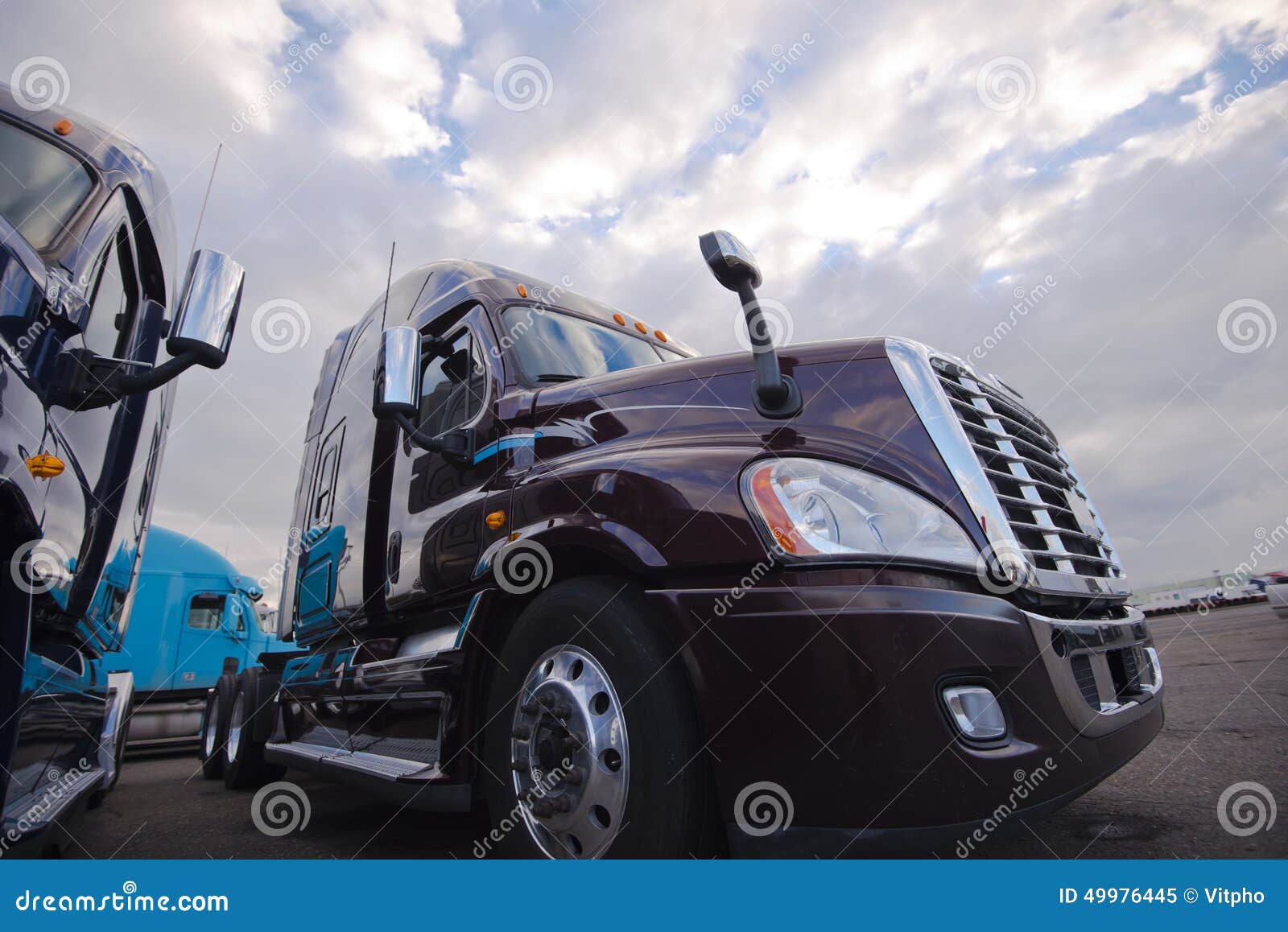 Rig semi trucks standing on trakstope on background cloudy sky. Modern big rigs semi trucks without trailers only tractors on sludge on a large parking area with reflection on glossy surfaces abutting body mirrors in a cloudy sky wavy.