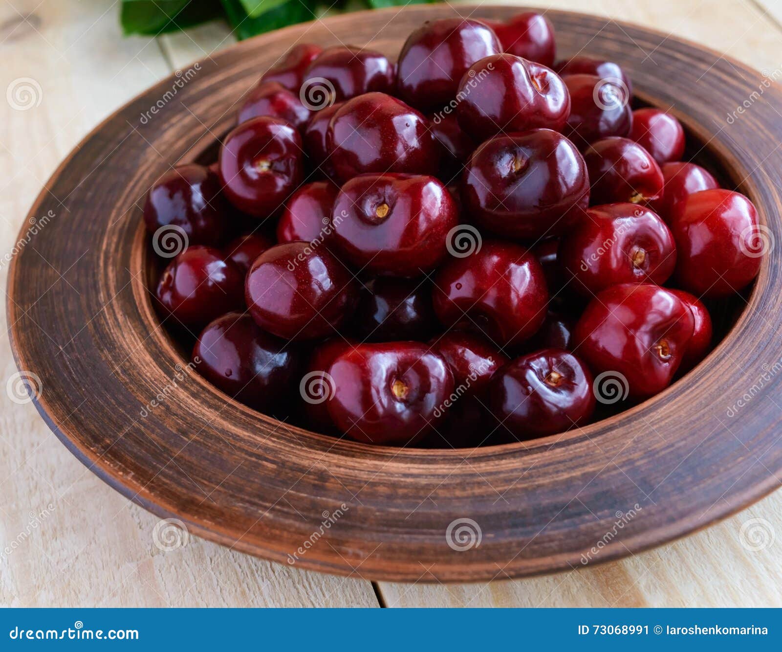 Ripe black cherries in a clay bowl on a light wooden background. Close-up.