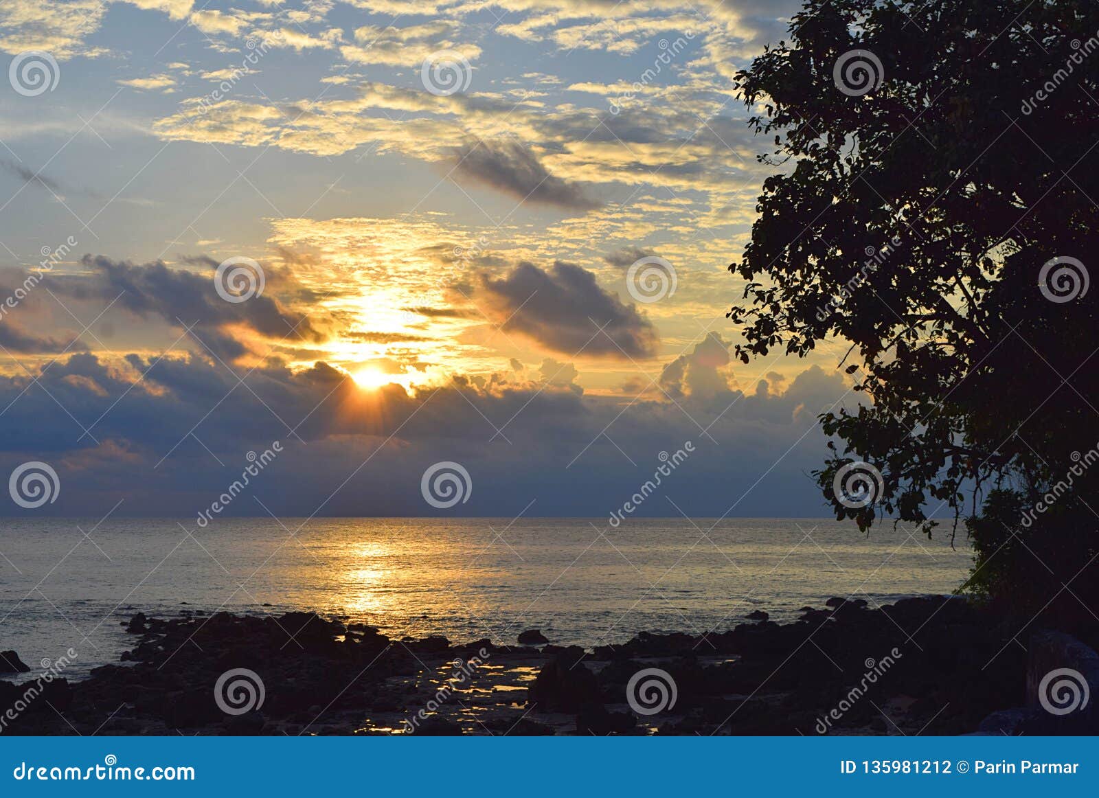 rising sun with golden sunshine with clouds in sky with lining over sea and contours of tree and stones - neil island, andaman