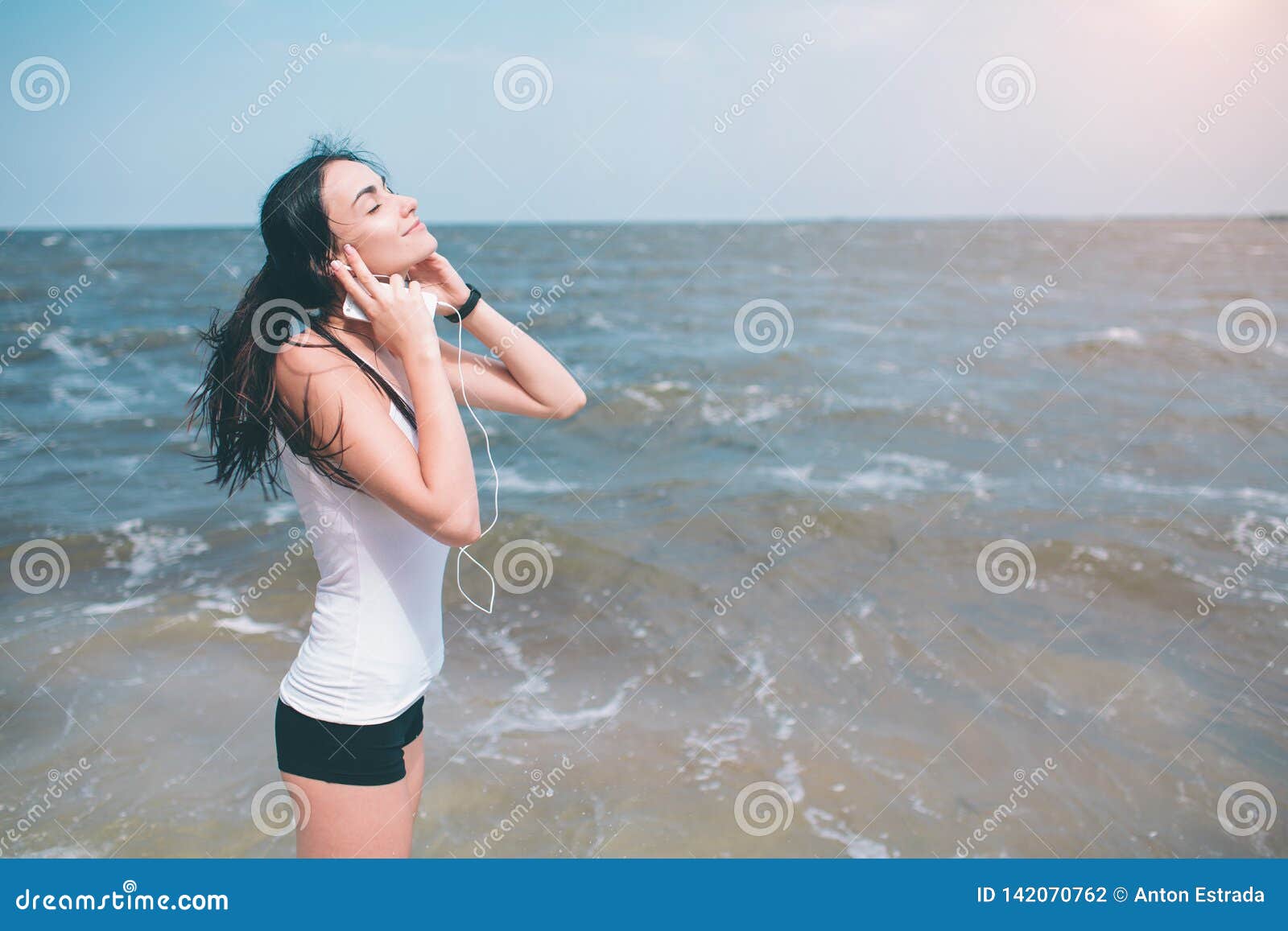 Ritratto di giovane donna sportiva in cuffie che si rilassano mentre sedendosi vicino all'oceano di estate, ascolto femminile att. Ritratto di giovane donna sportiva in cuffie che si rilassano mentre sedendosi vicino all'oceano di estate, musica favorita d'ascolto femminile attraente durante il tempo di ricreazione nel fine settimana