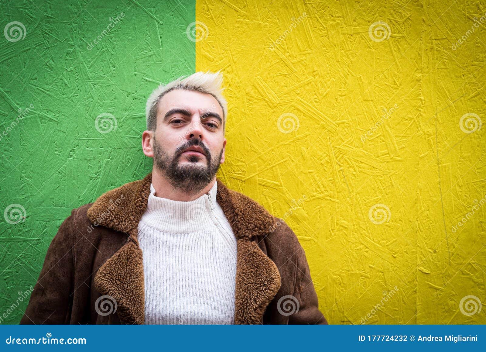 portrait of a hipster with platinum blond hair and dark beard, wearing a white sweater and a brown coat, green and intense yellow