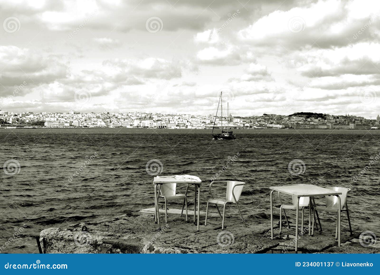 river boat on the lisbon background. yellow chairs and tables in riverside cafe in almada. portugal.