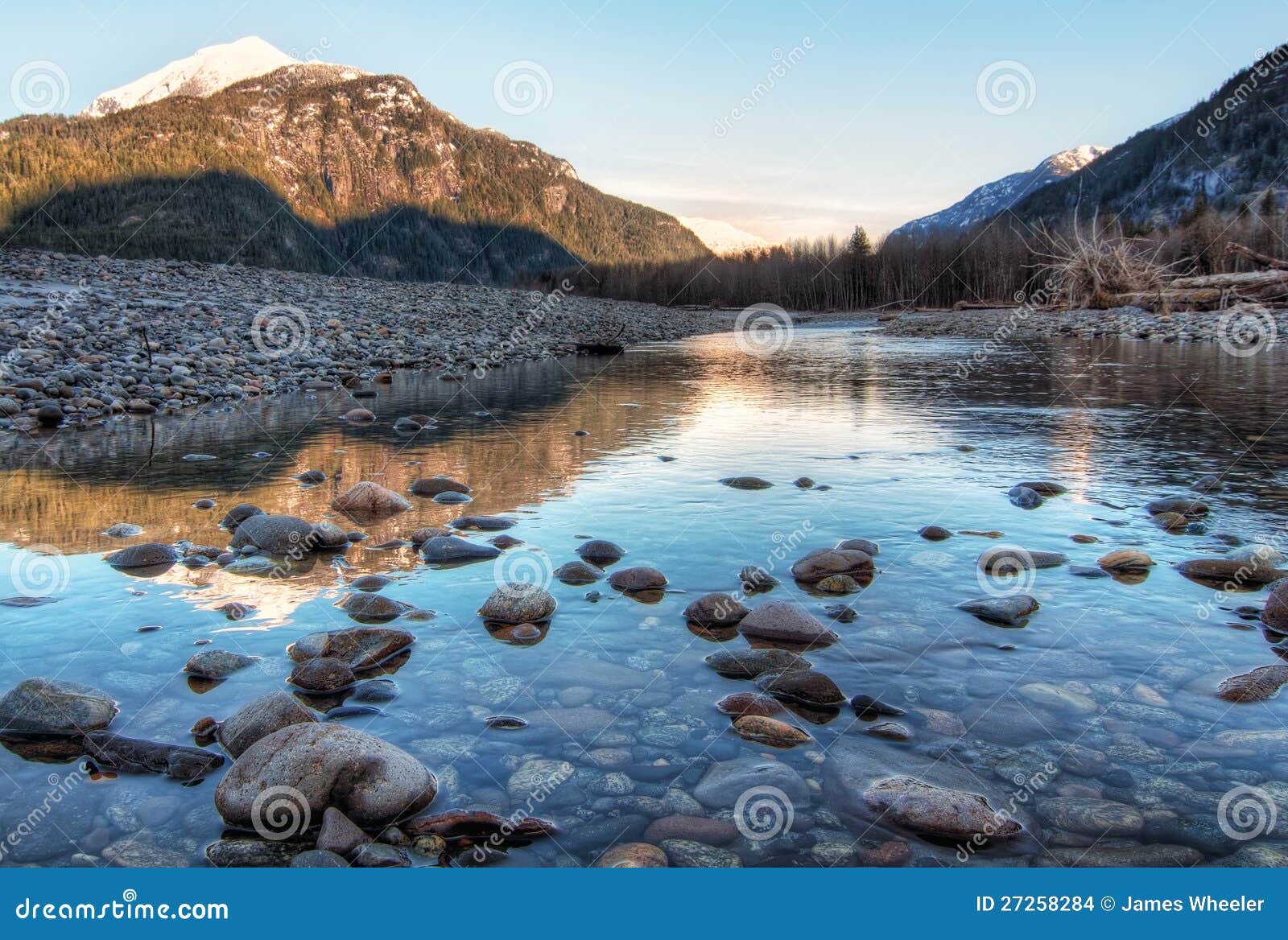 River Leading Towards Sunset Lit Mountains. Clear river with rocks leads towards mountains lit by sunset