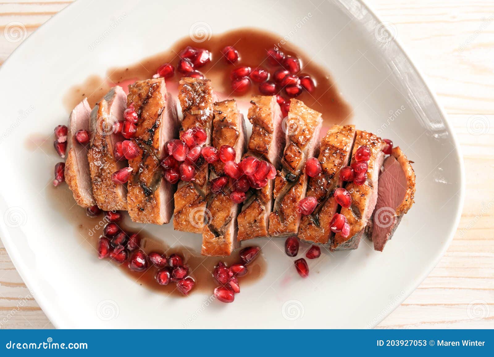 roasted duck breast with pomegranate seeds and sauce on a white plate for a festive meal, high angle view from above