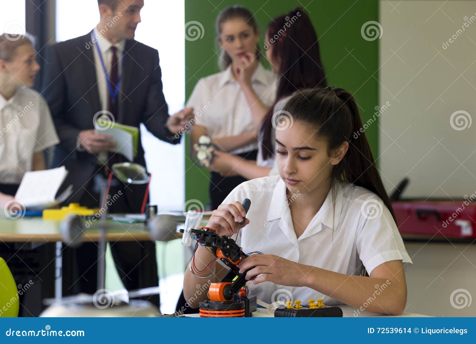 Robotic teknologi i skola. Skola flickan som arbetar på byggande av en robotic arm i hennes skolakurs En grupp av studenter kan ses i bakgrunden som talar till en lärare