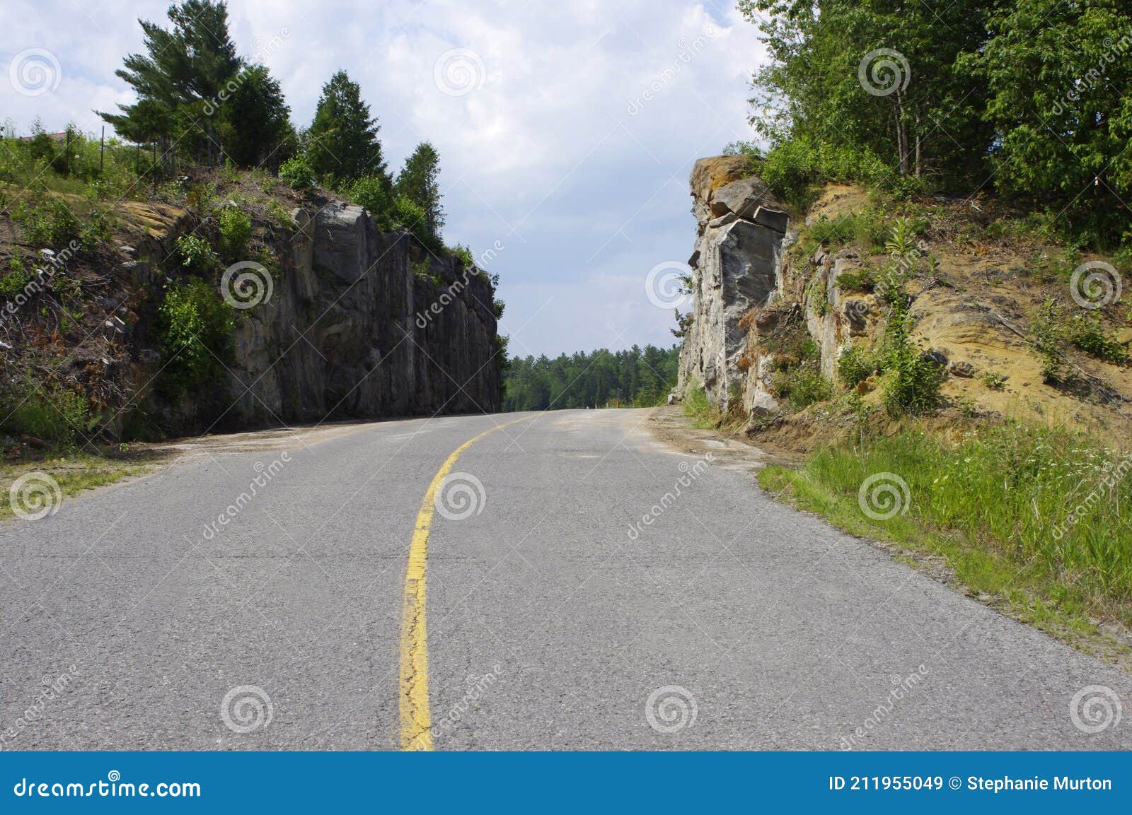 Rock Cliff Wall beside Smooth Paved Road with Yellow Solid Line Stock