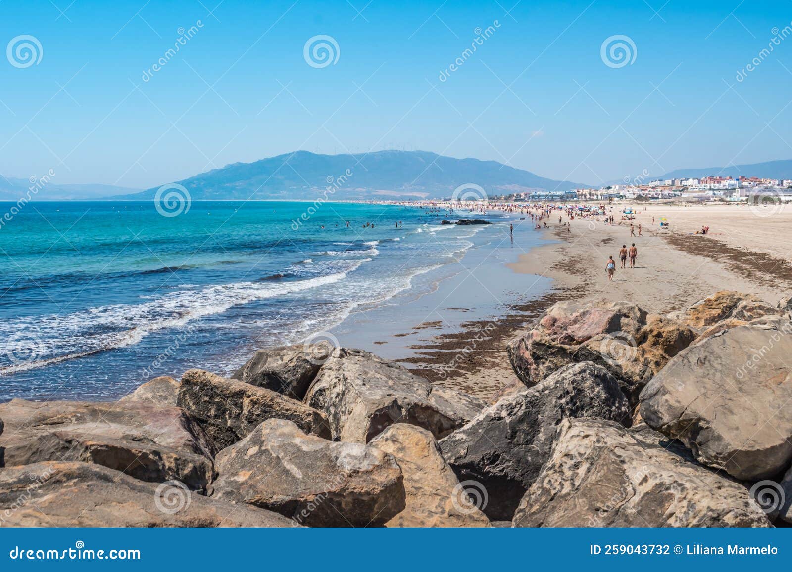 rocks overlooking the sand and sea of los lances beach, silhouettes of bathers and mountain in the background, tarifa spain