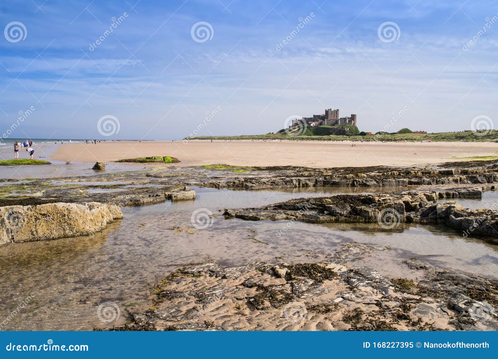 the rocky foreshore and sandy beach with bamburgh castle in the background
