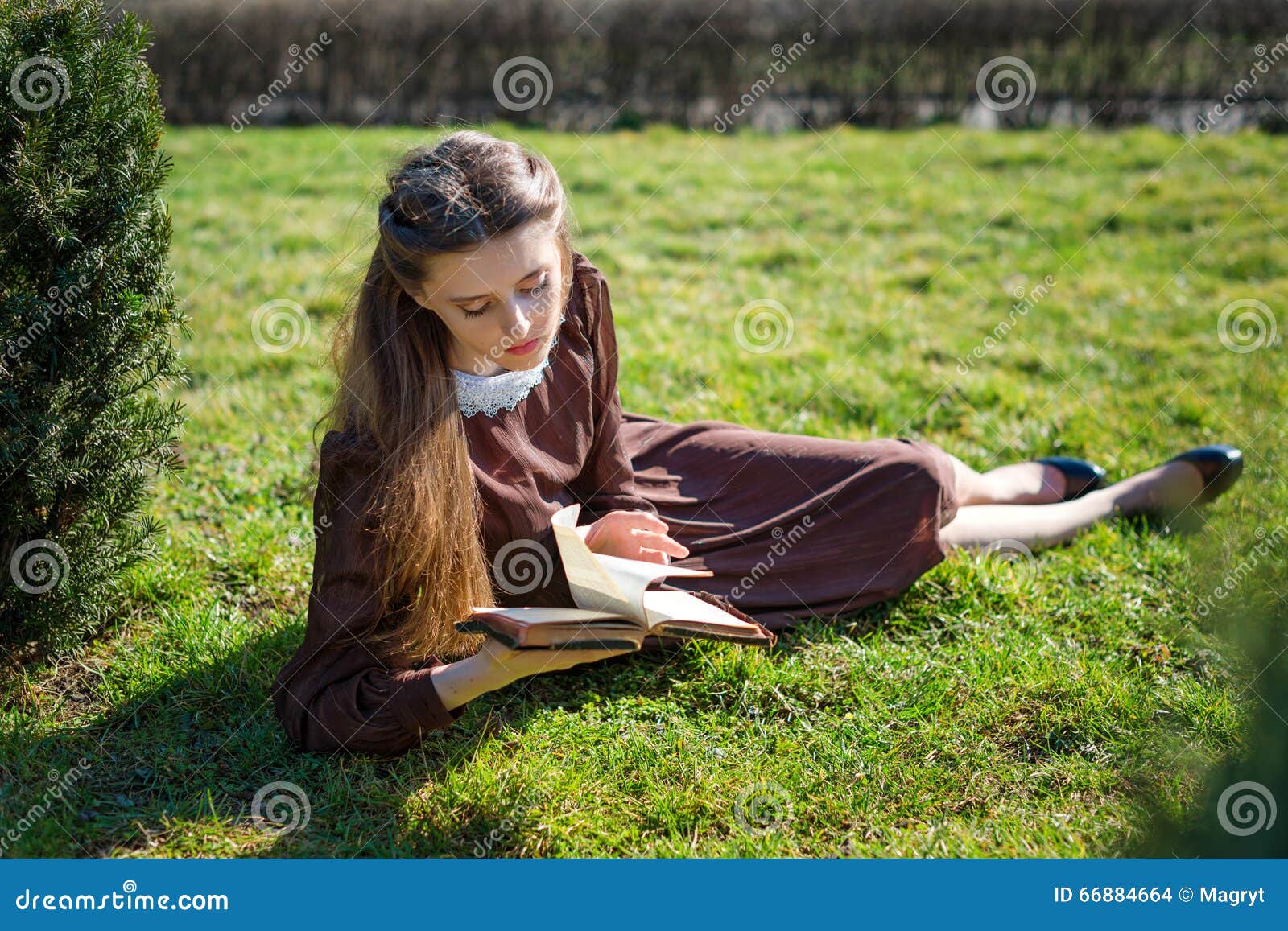 Romantische jonge vrouw die een boek in de tuinzitting lezen op het gras Ontspan openluchttijdconcept