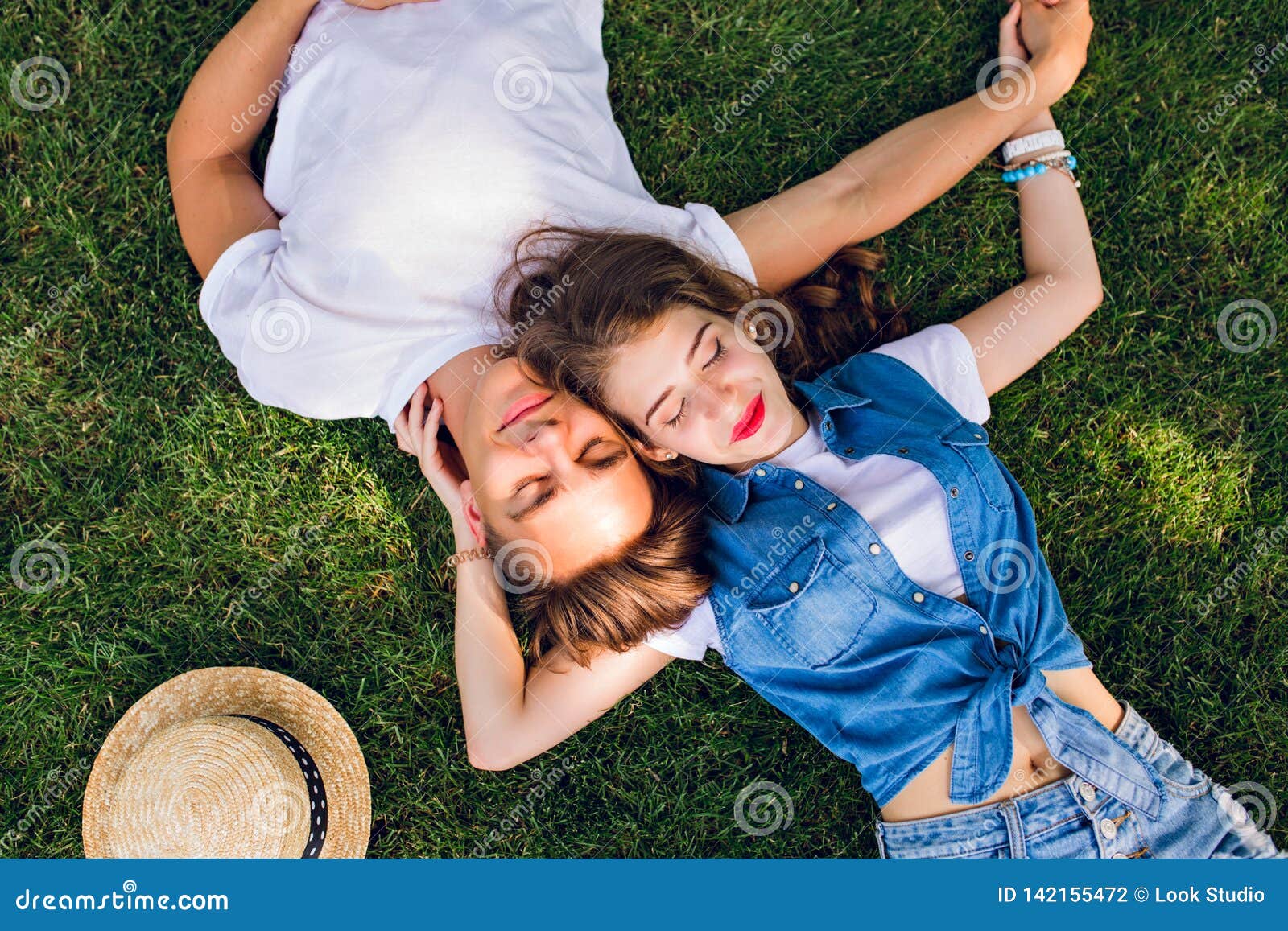 Romantische Paare von den jungen Leuten, die auf Gras im Park liegen Sie legen auf die Schultern von einander und halten Hände zusammen