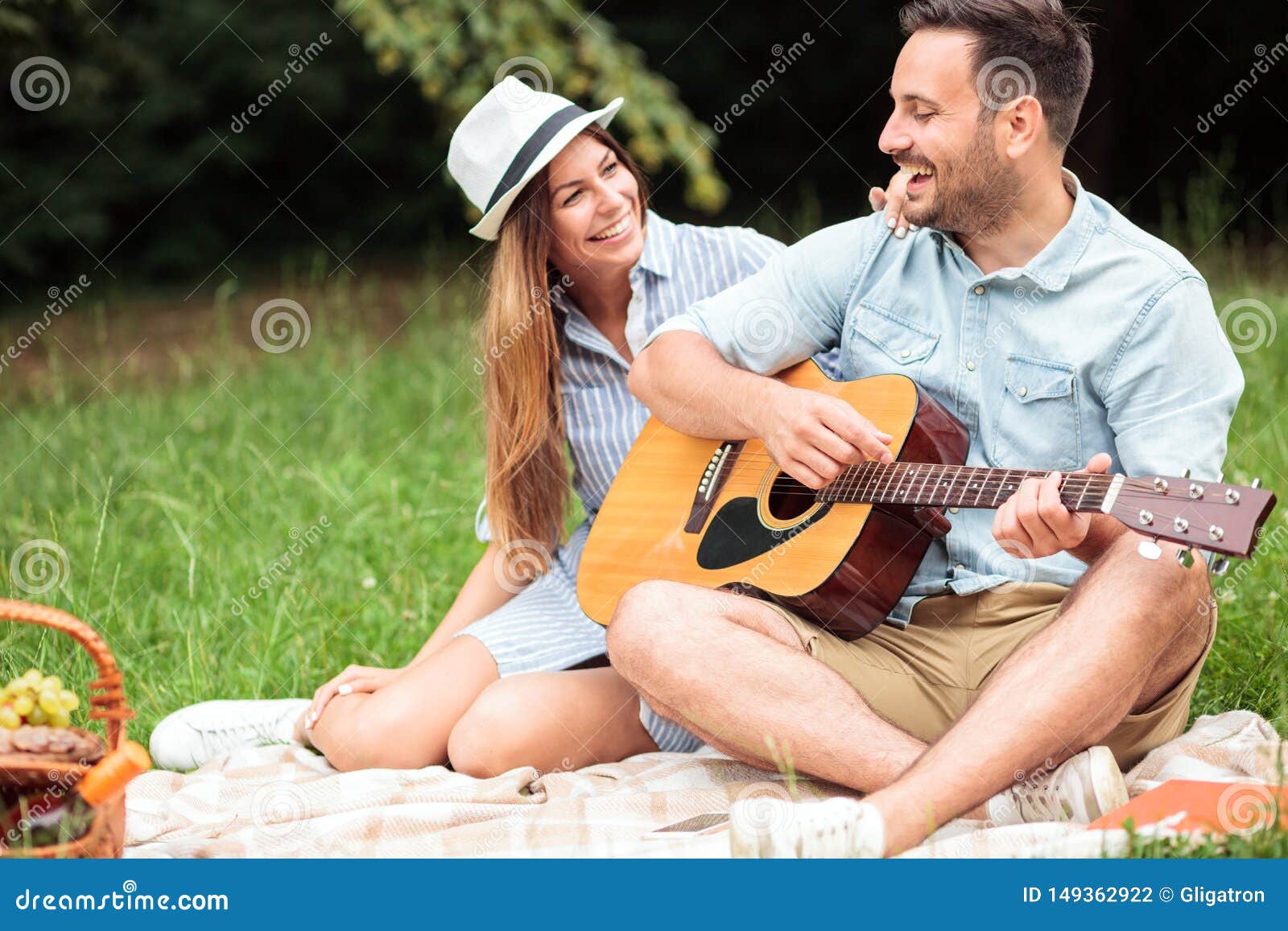 Romantiska unga par som har en stor tid på en picknick och att spela gitarren och att sjunga. Härliga lyckliga unga par som tycker om deras tid i, parkerar Sitta på en picknickfilt och att spela gitarren och att sjunga