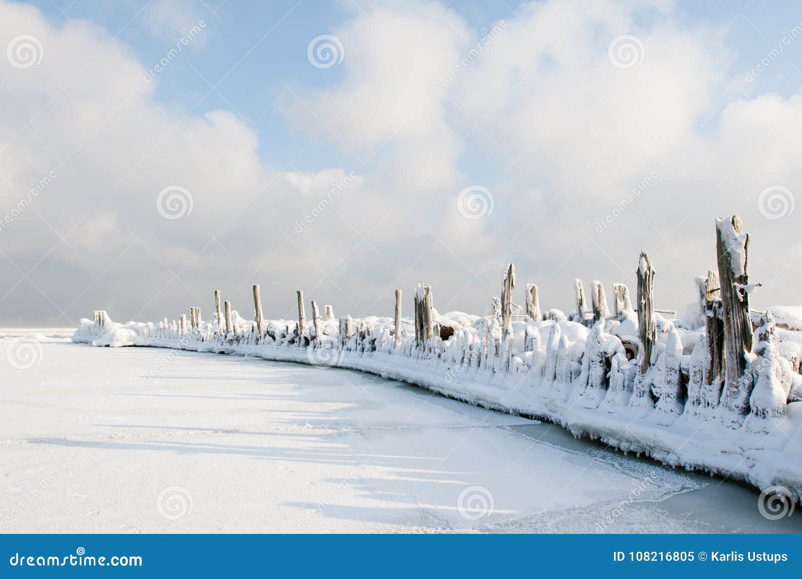 Rompeolas viejo cubierto en nieve. Engure, Letonia Rompeolas viejo del puerto de Engure cubierto en nieve e hielo en fondo del cielo nublado